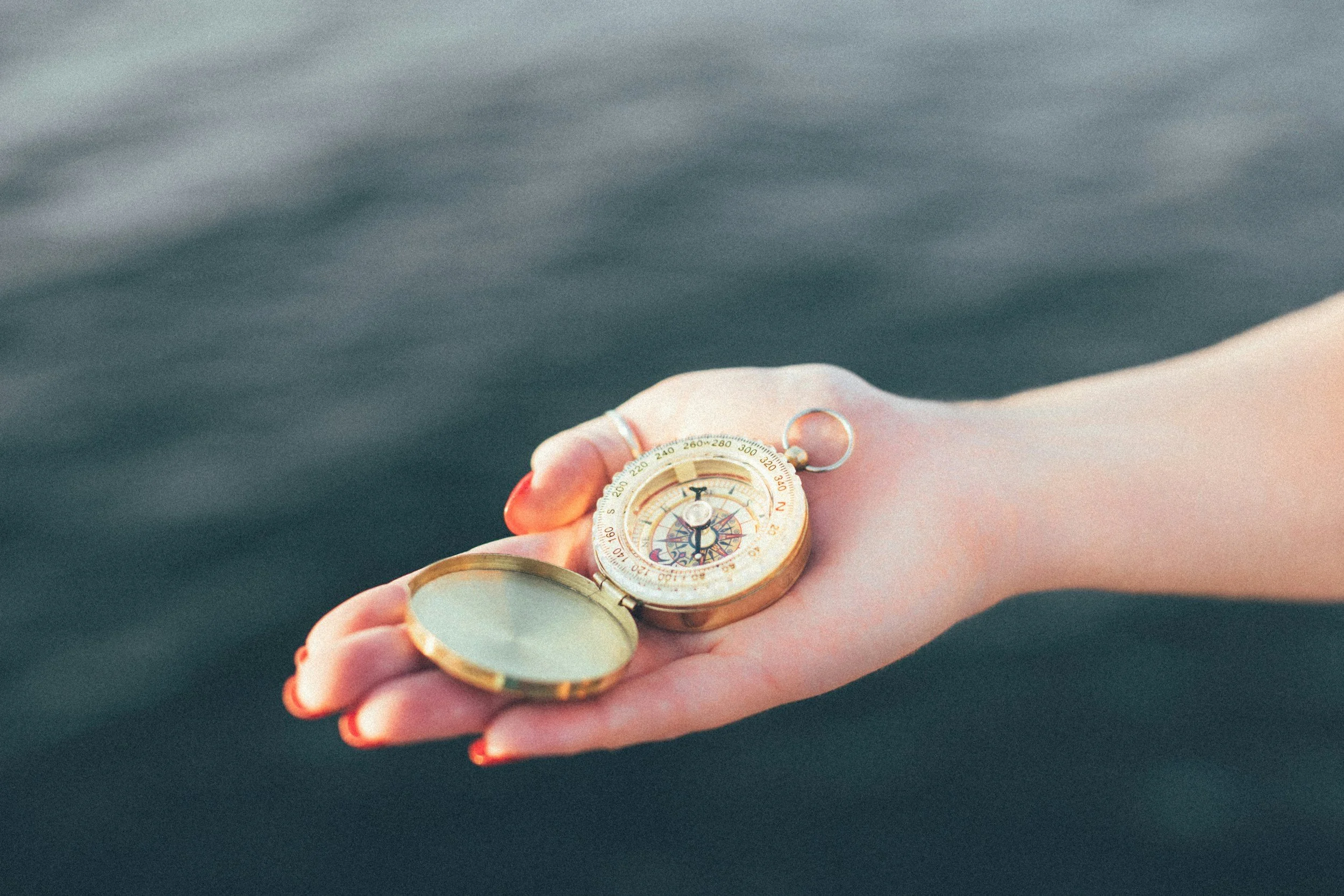 A woman holds a compass in her hand, with deep water in the background.