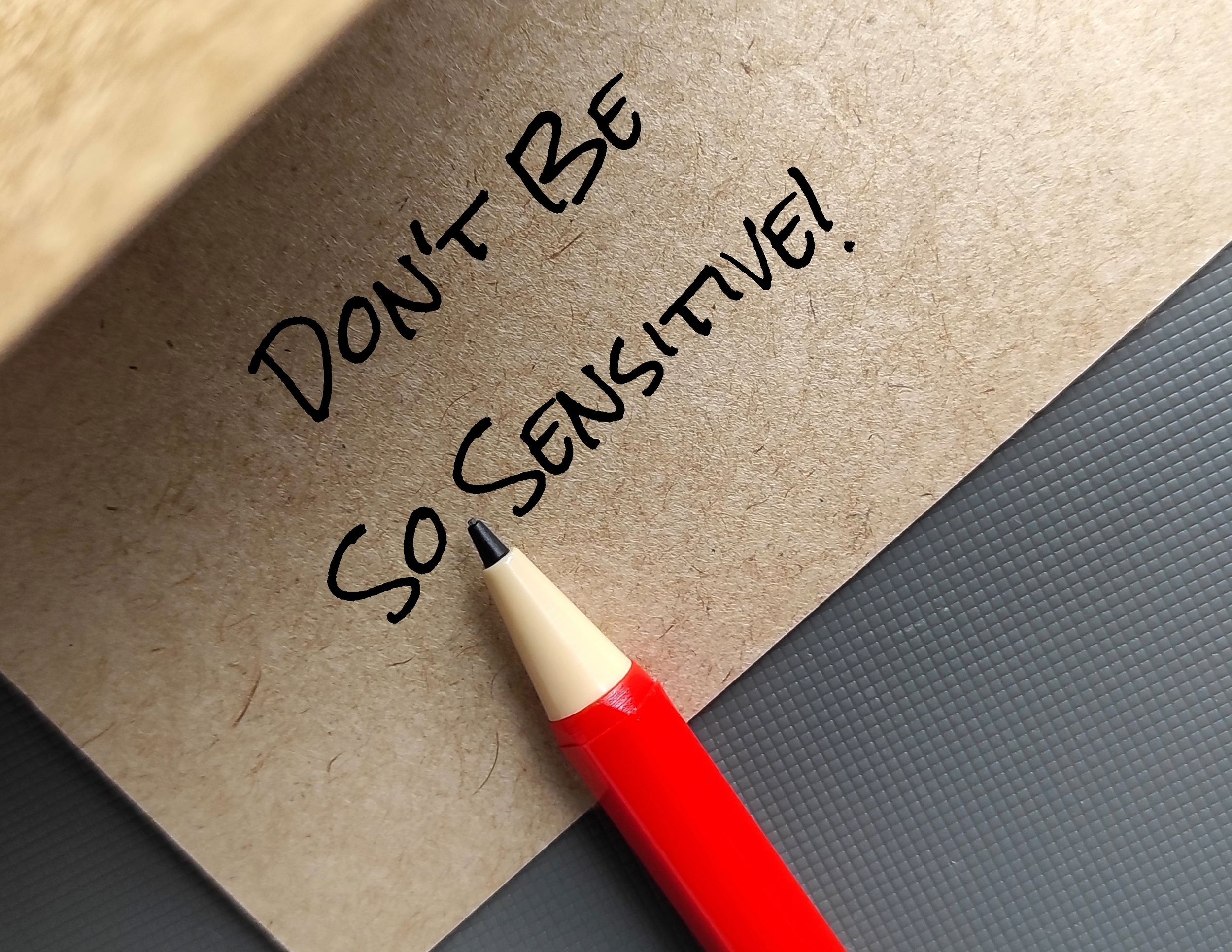 an envelope with the message 'don't be so sensitive' exclaimation mark, with a pencil resting below it.