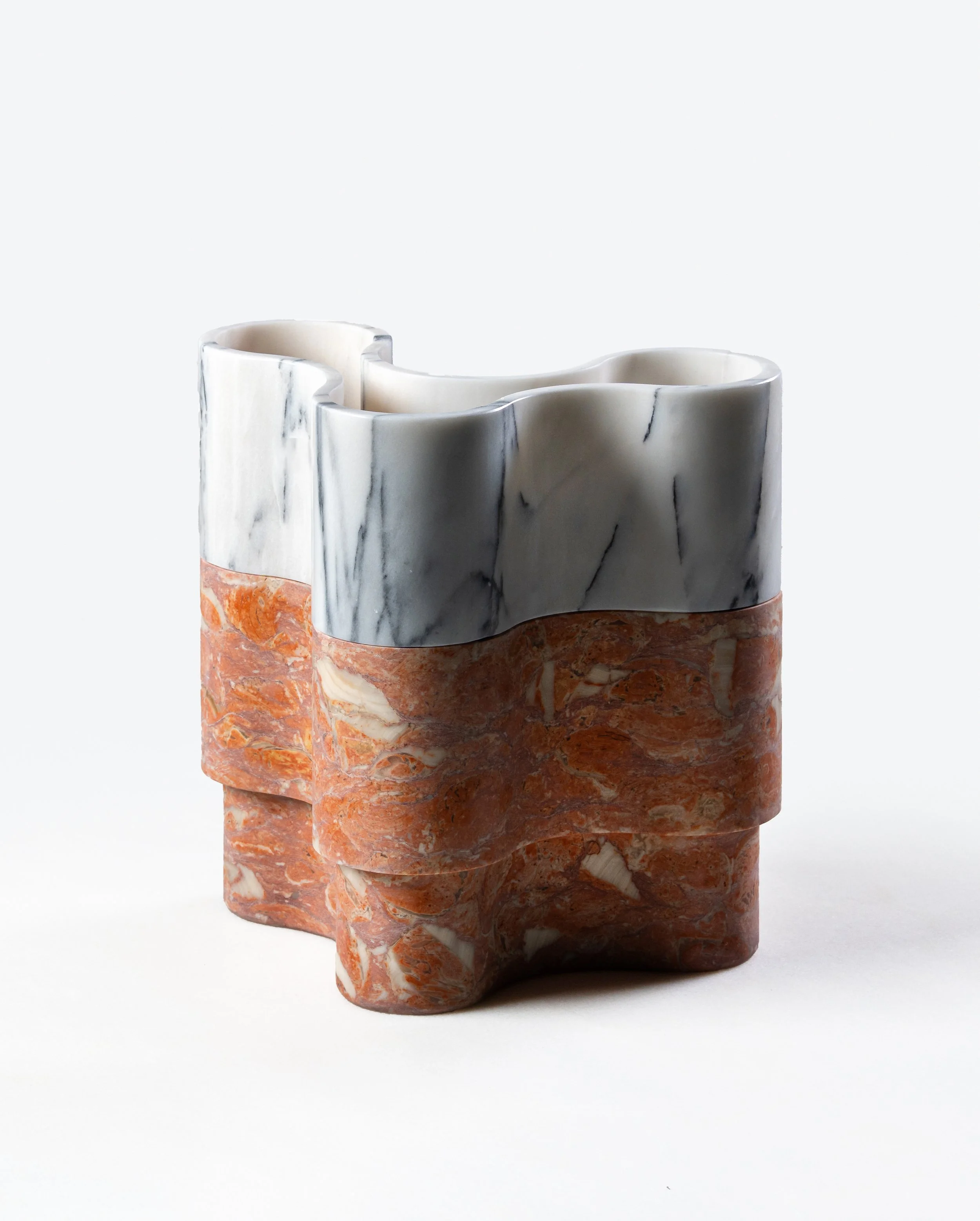 A marble and stone sculpture with multiple layers and textures, featuring a band of reddish-orange stone at the bottom, layered with white marble in the middle, topped by a smooth, curved white marble piece, against a plain white background.