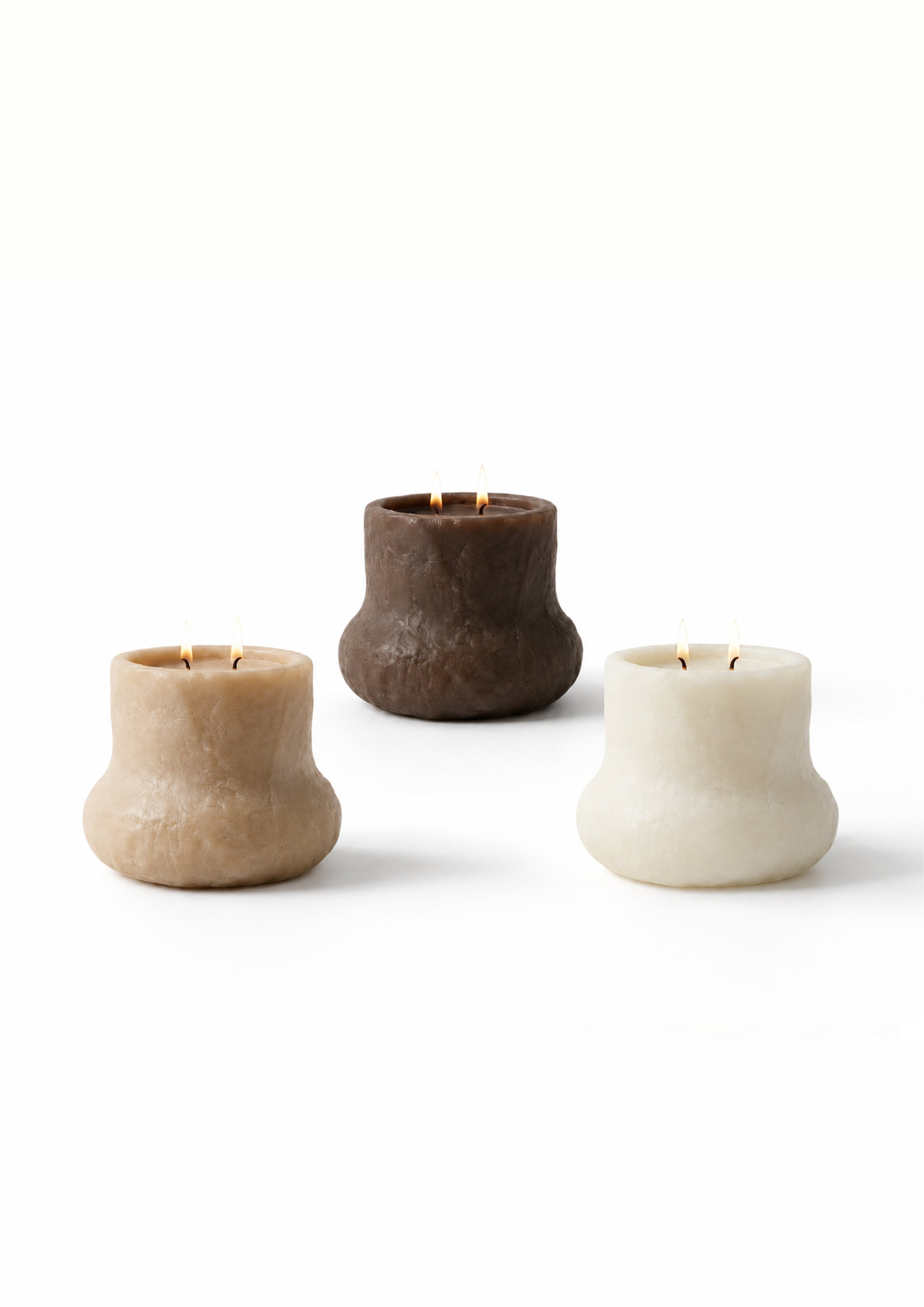 Three candles in different colors—beige, dark brown, and white—set against a plain white background, each lit with a small flame.