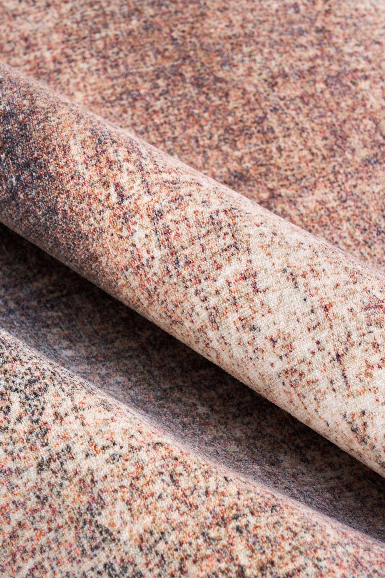 Close-up of rolled multi-colored speckled fabric with pink, beige, and black threads.