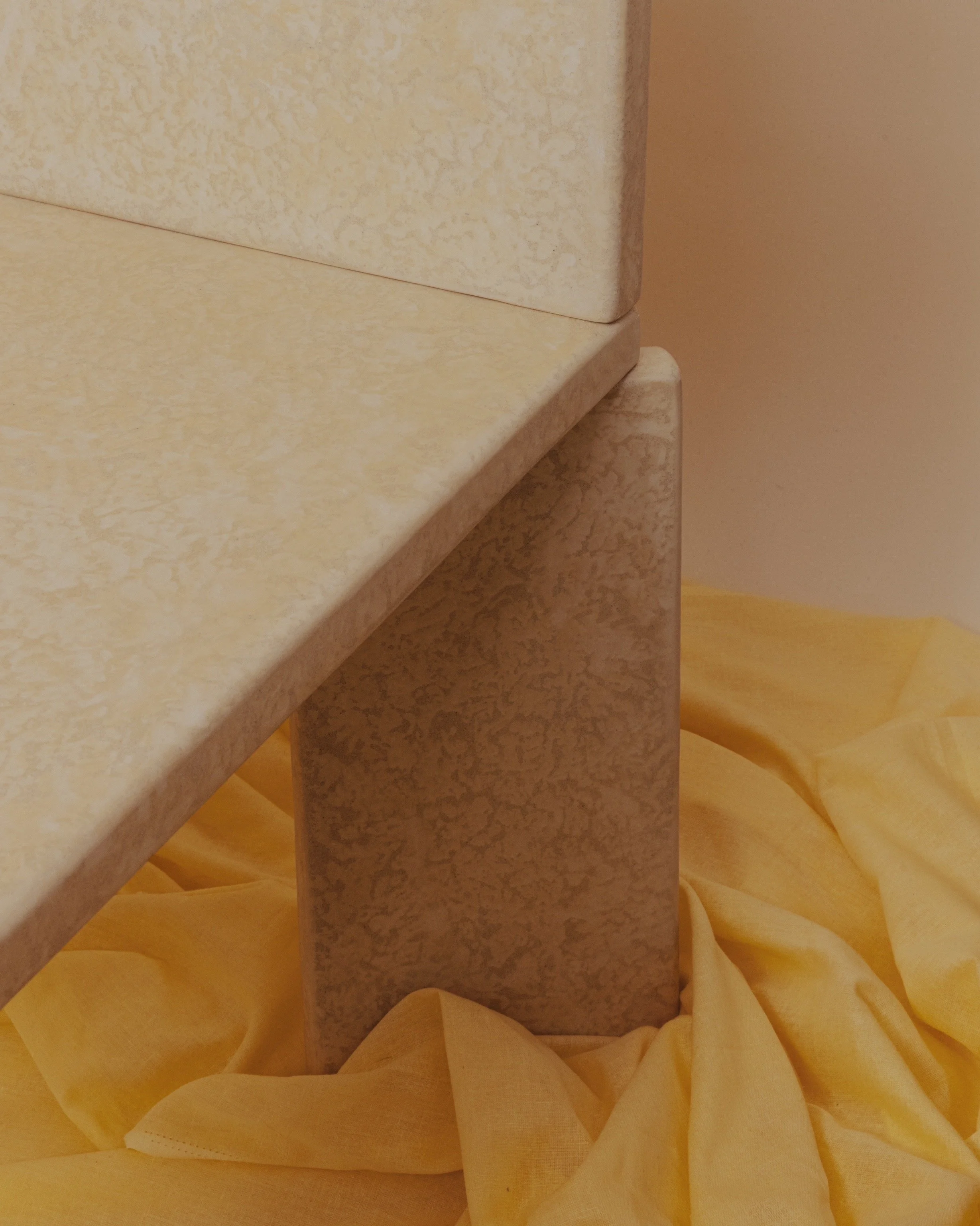 Close-up of beige marble columns with yellow fabric draped underneath.