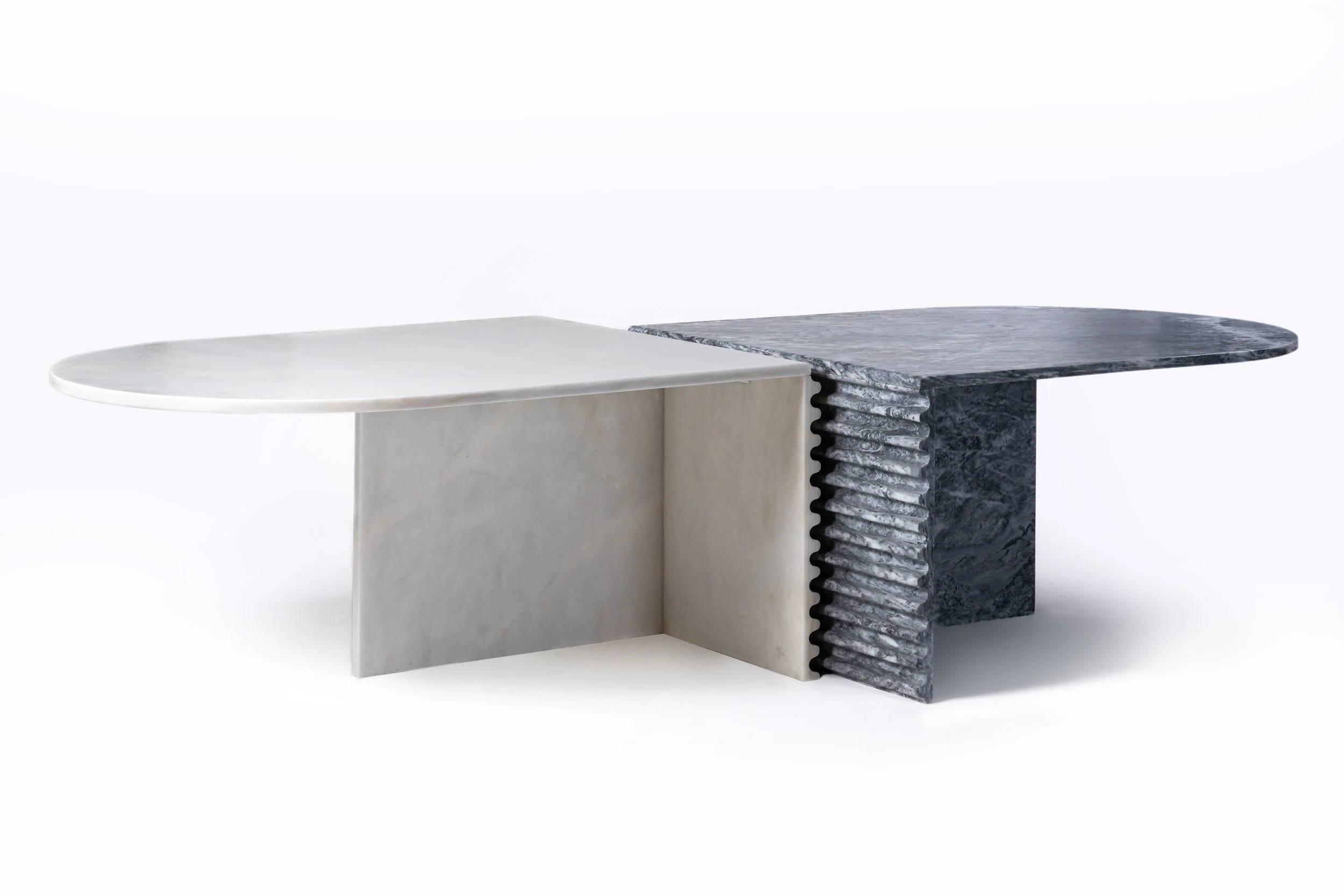 A modern, minimalist table with two contrasting marble surfaces: one white and the other black with gray veining, supported by sculptural bases.