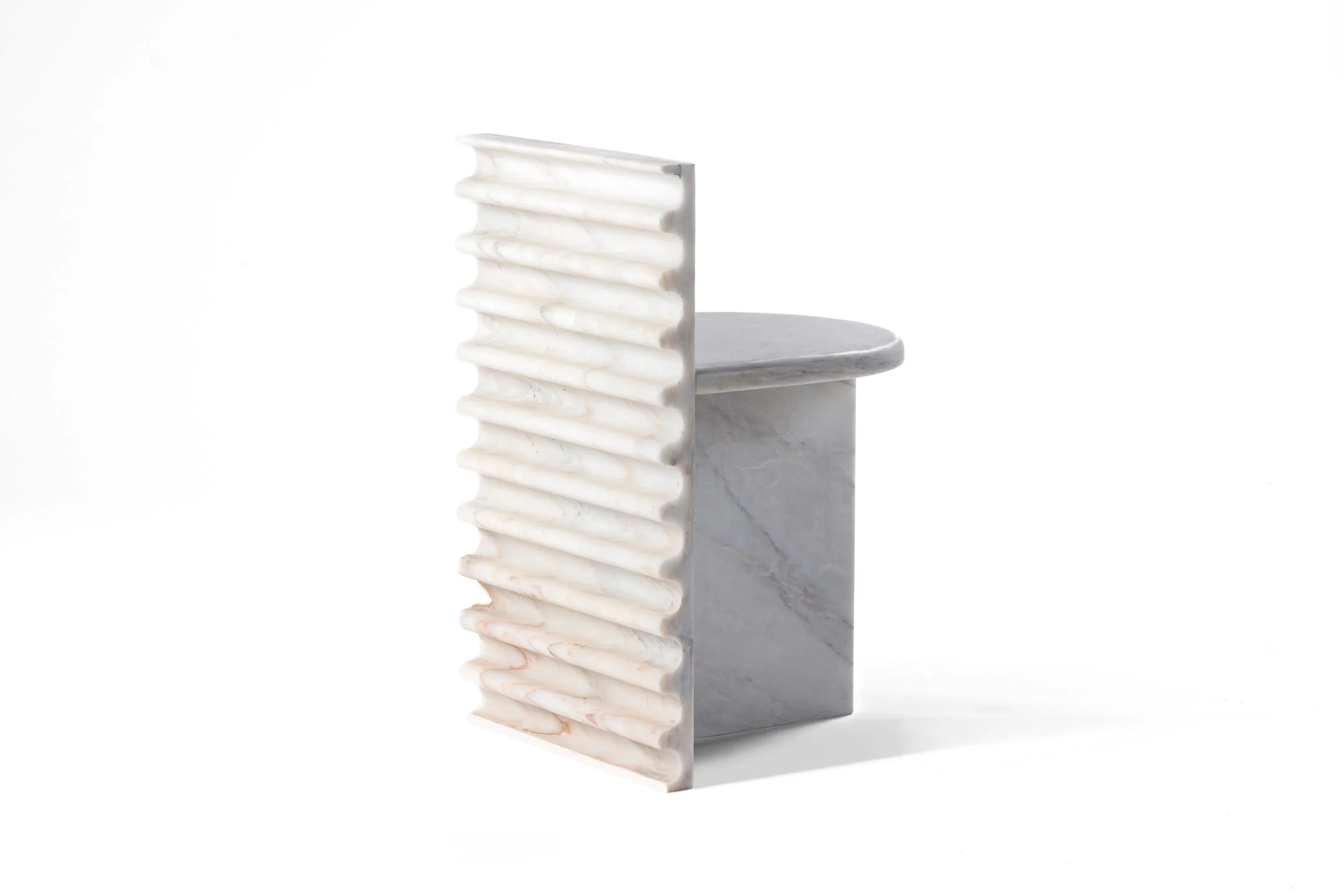A modern white marble sculpture with a vertical ridged design, supported by a marble base and a flat circular marble platform.