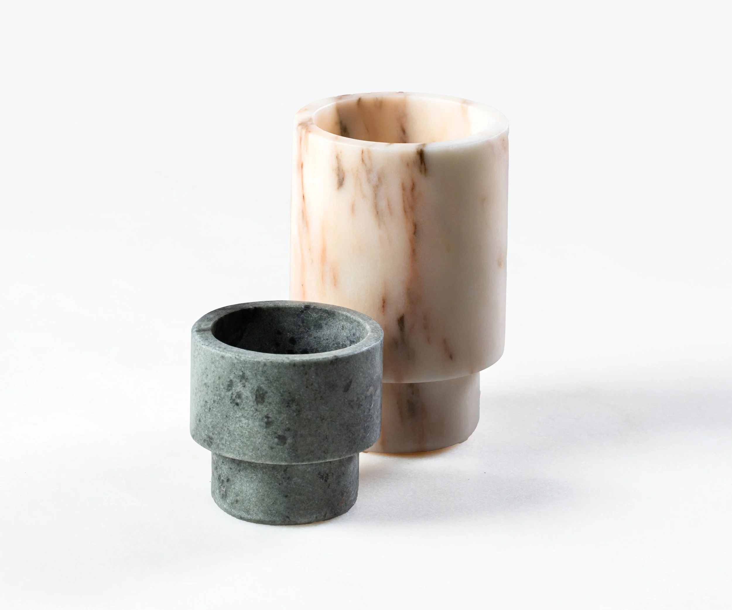 A small gray stone cup and two taller marble cups with brown and beige veining on a white background.
