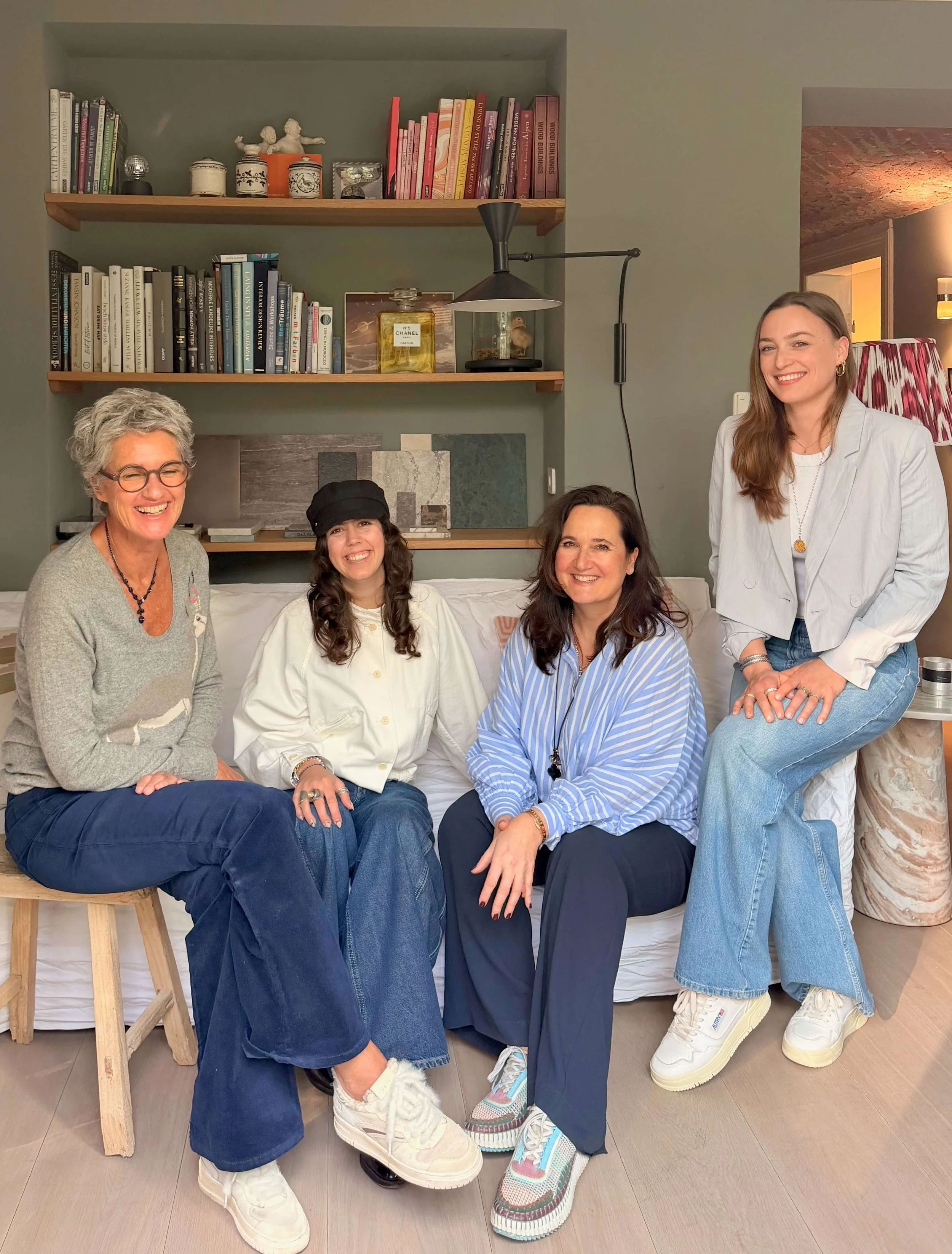 Fünf Frauen sitzen und stehen lächelnd auf einem Sofa in einem Wohnzimmer vor einer Bücherwand.