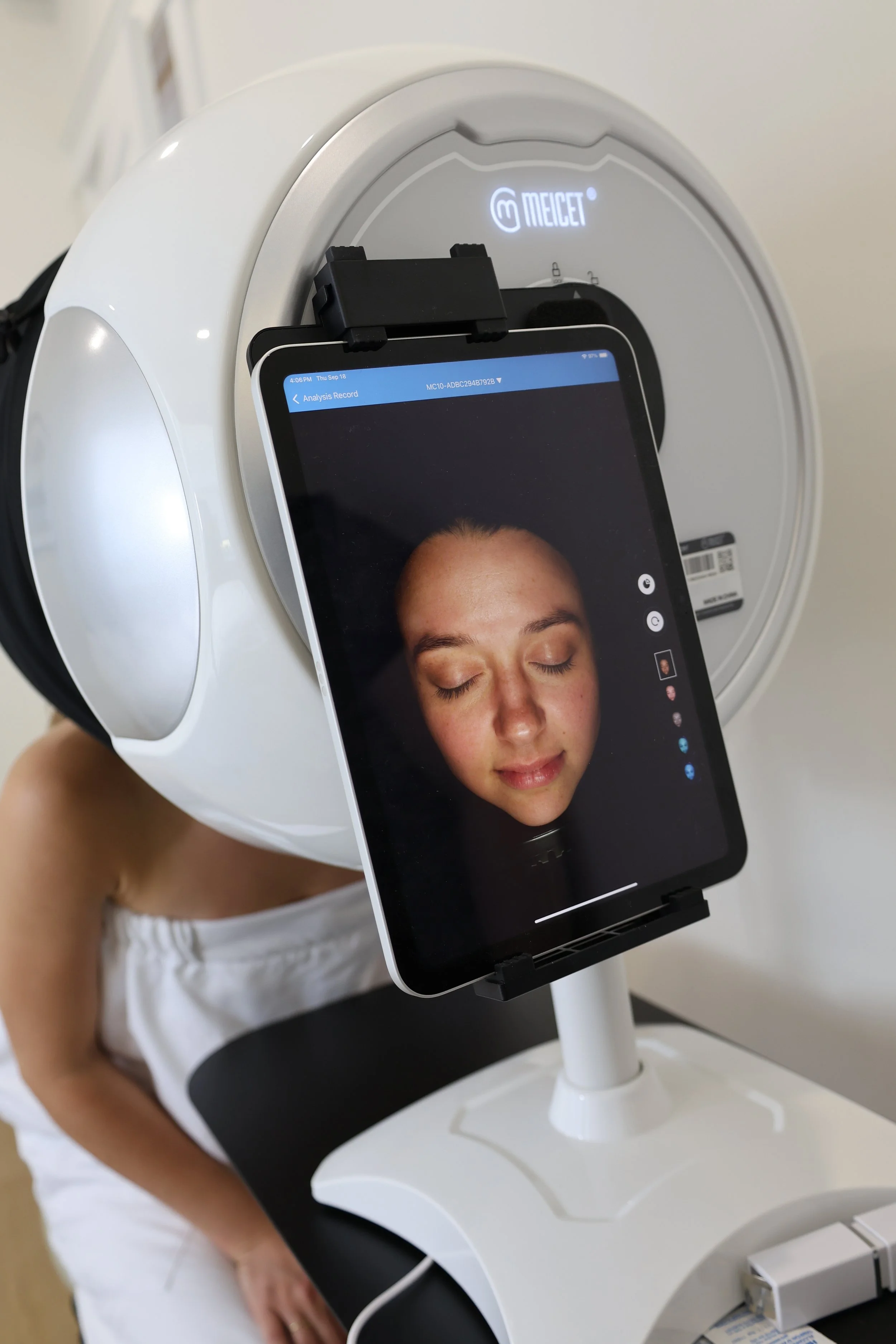 A woman undergoing a medical scan with her face on a tablet screen showing her face with closed eyes, placed in front of a medical imaging device.