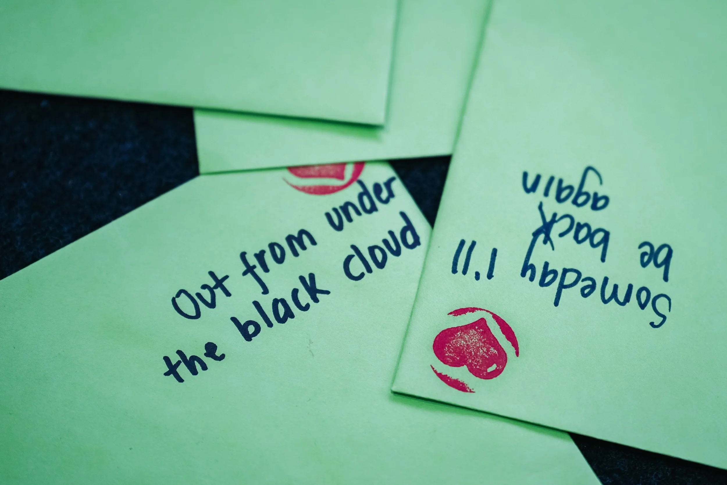 Light green paper notes with handwritten messages. One says, 'Out from under the black cloud.' The other says, 'Friday, 11! I am so sad.' with a red heart stamp.
