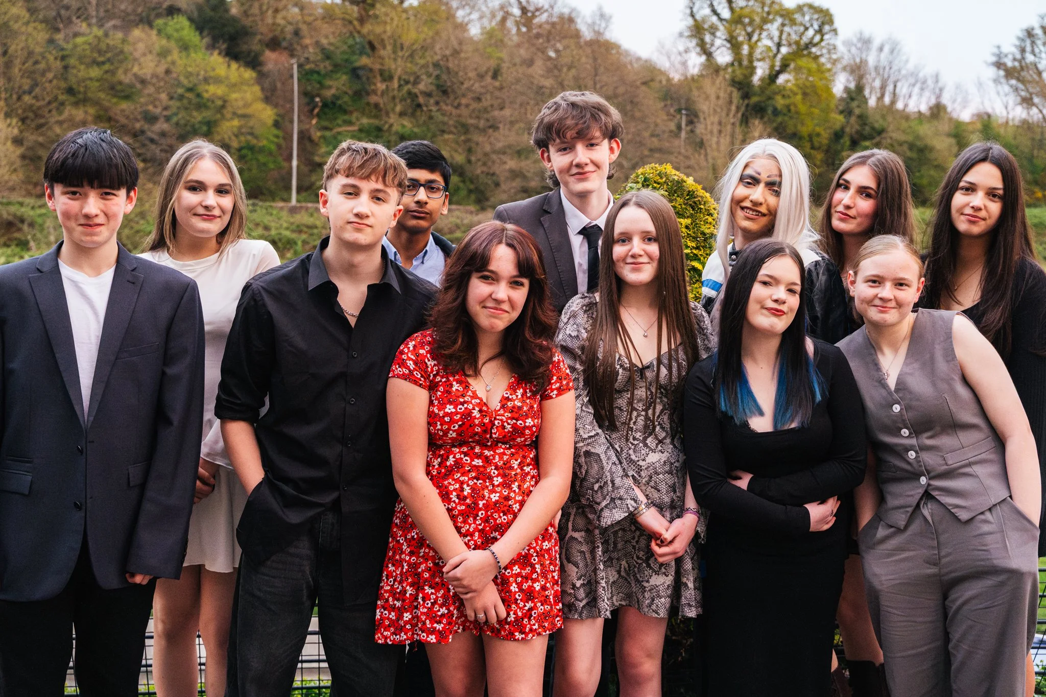 A group of young people dressed stylishly, posed outdoors in front of a scenic background of trees and hills.