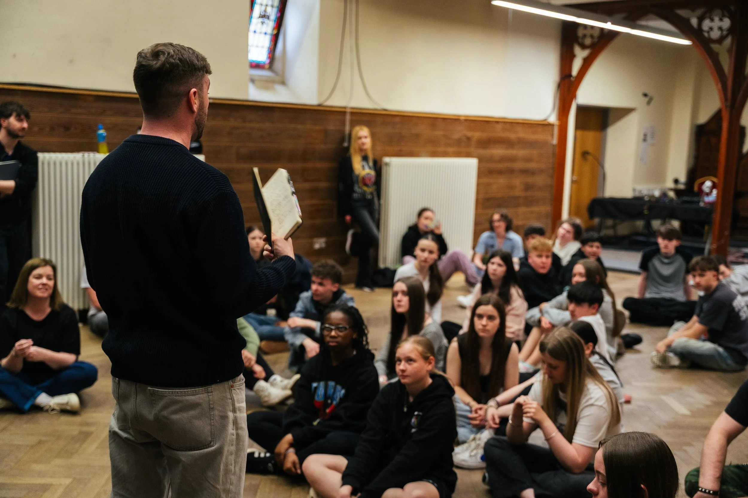 A man reading a book to a group of children sitting on the floor in a room.