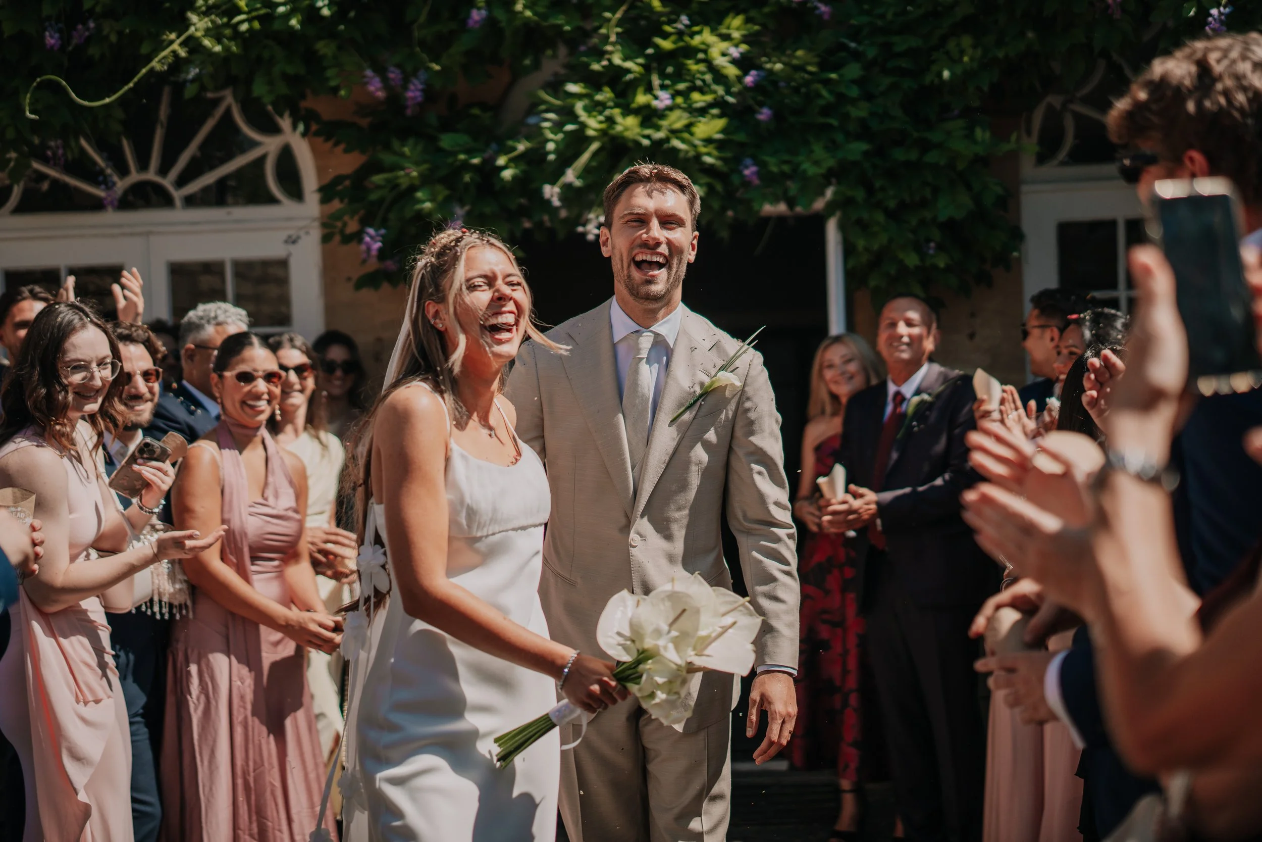 Happy bride and groom laughing at their wedding outdoor celebration, surrounded by friends and family.