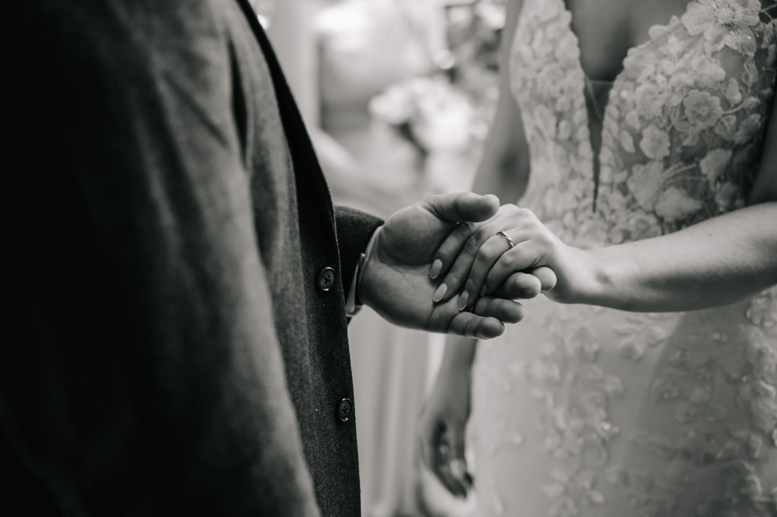 Close-up of a couple holding hands during their wedding ceremony, with the bride's hand resting on the groom's hand, both wearing wedding rings.