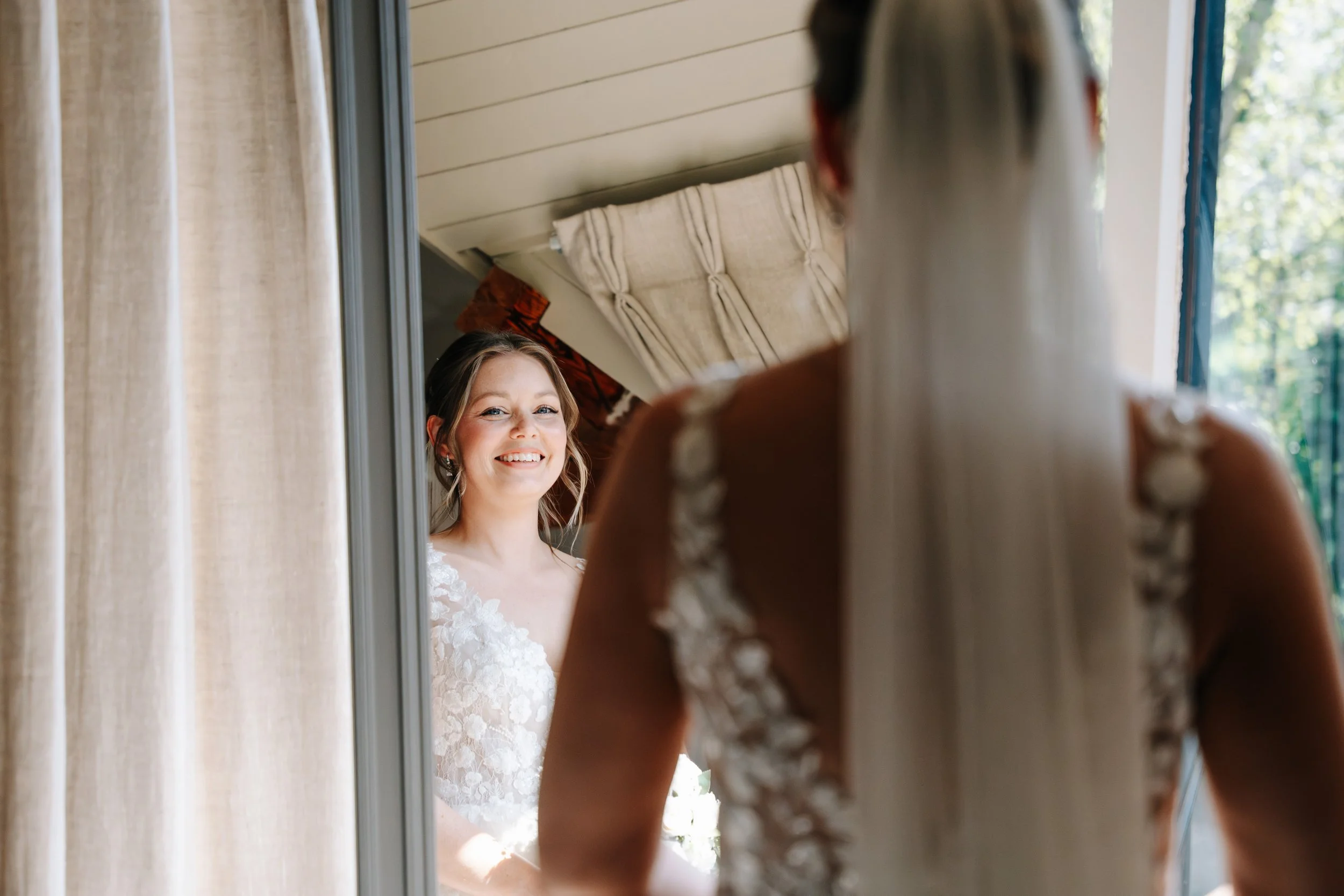 A bride looking at herself in a mirror, smiling, as she prepares for her wedding day.