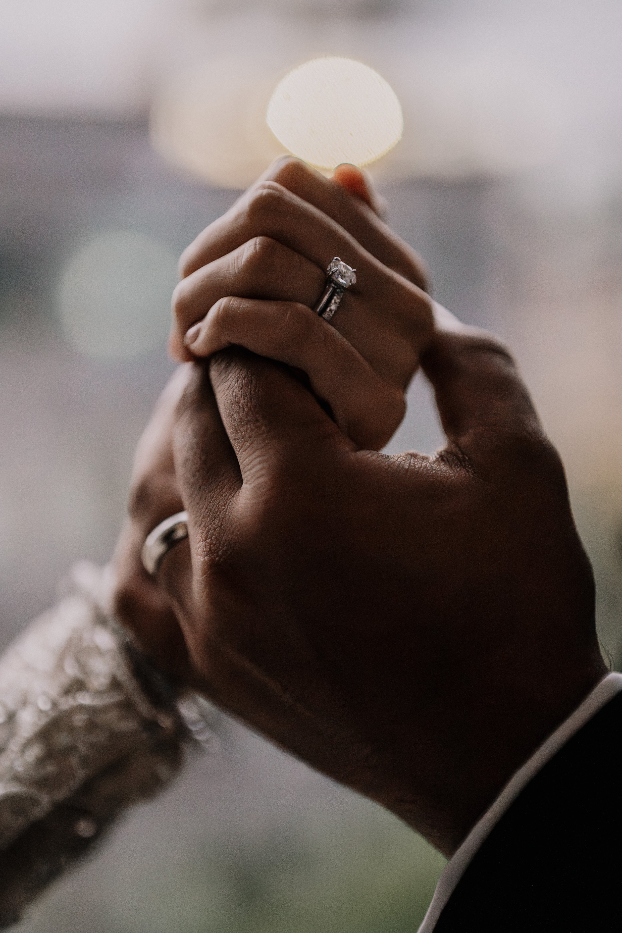 Close-up of a couple holding hands, showing wedding rings, with blurred background.