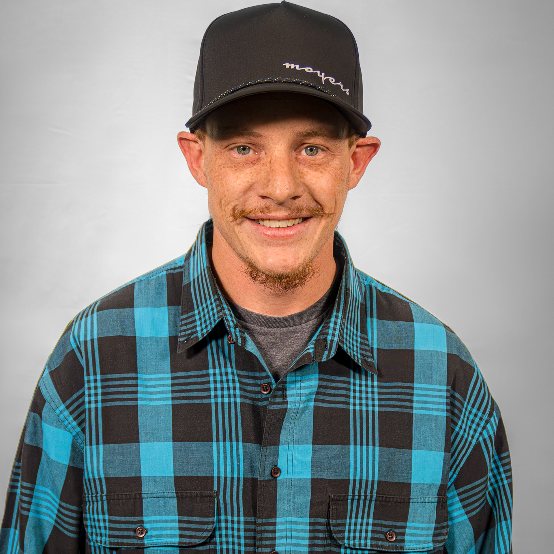 Person wearing a black cap and blue plaid shirt smiling