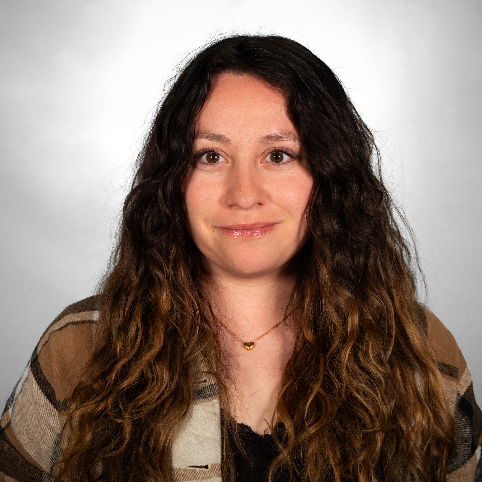 A young woman in a brown plaid jacket with a black undershirt. She has long curly brown hair. 