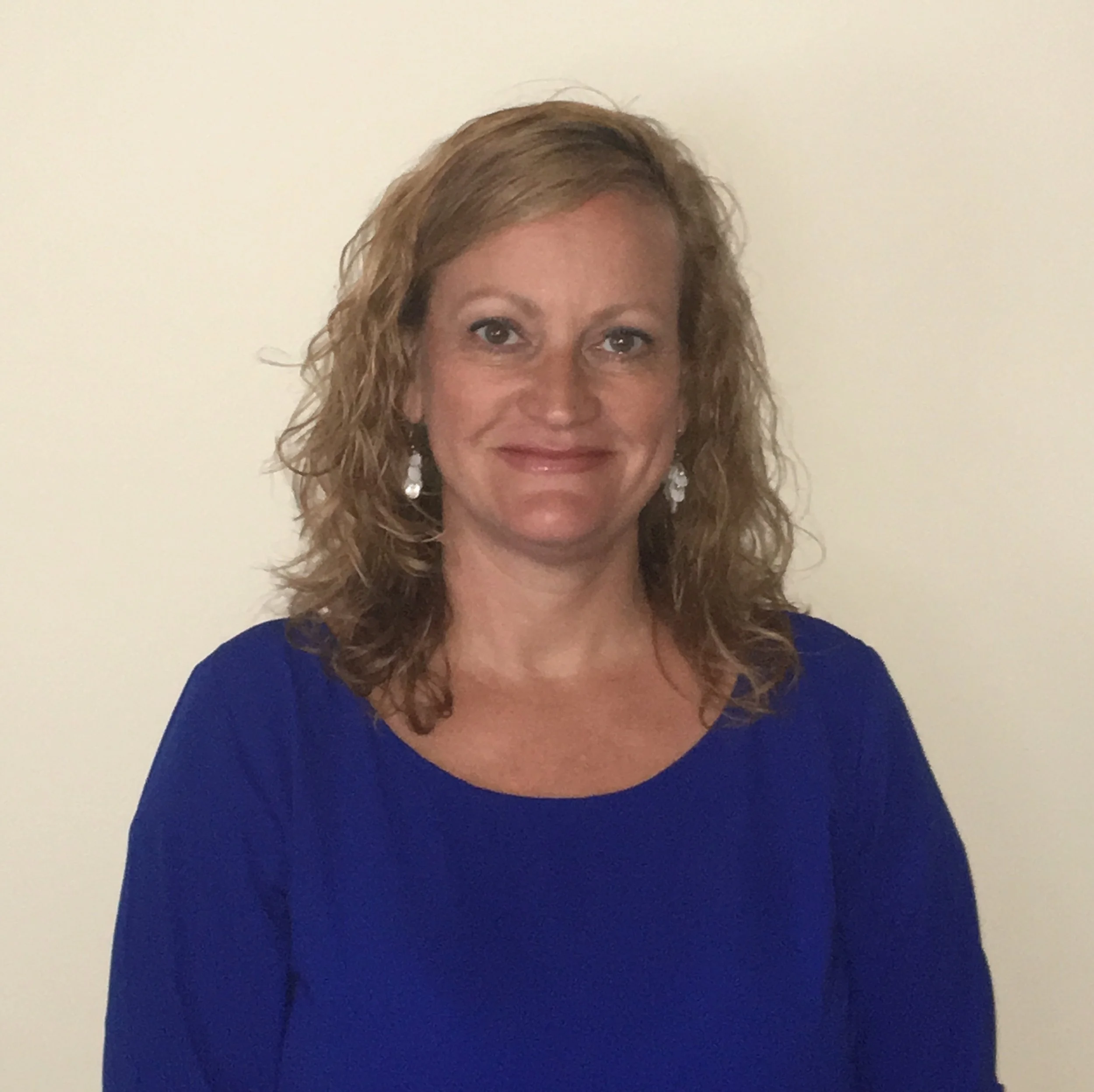Smiling woman with straight, light brown hair wearing a dark blue blouse against a light blue background.