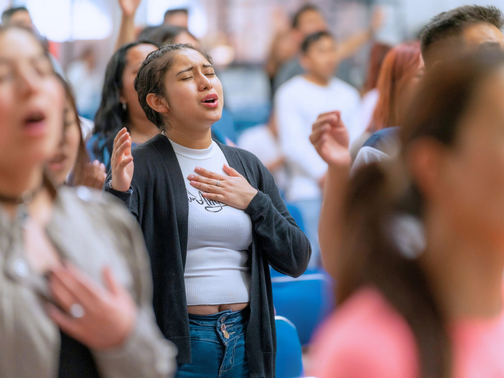 Young woman with hand on chest, eyes closed, singing or praying during a religious gathering or service.