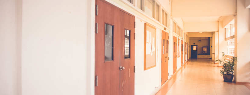 School hallway with wooden classroom doors and bulletin boards on the wall.