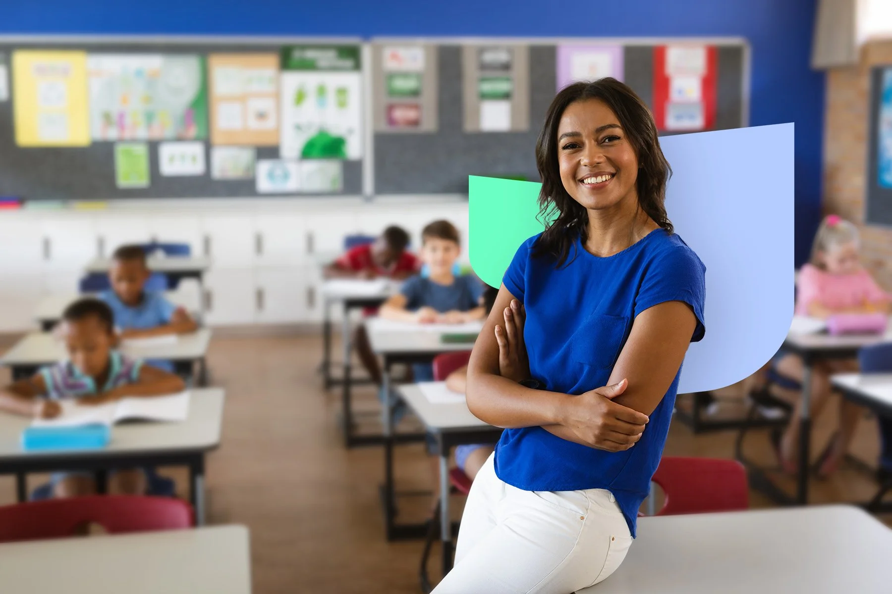 Happy female teacher in blue blouse leaning against a table in the classroom.