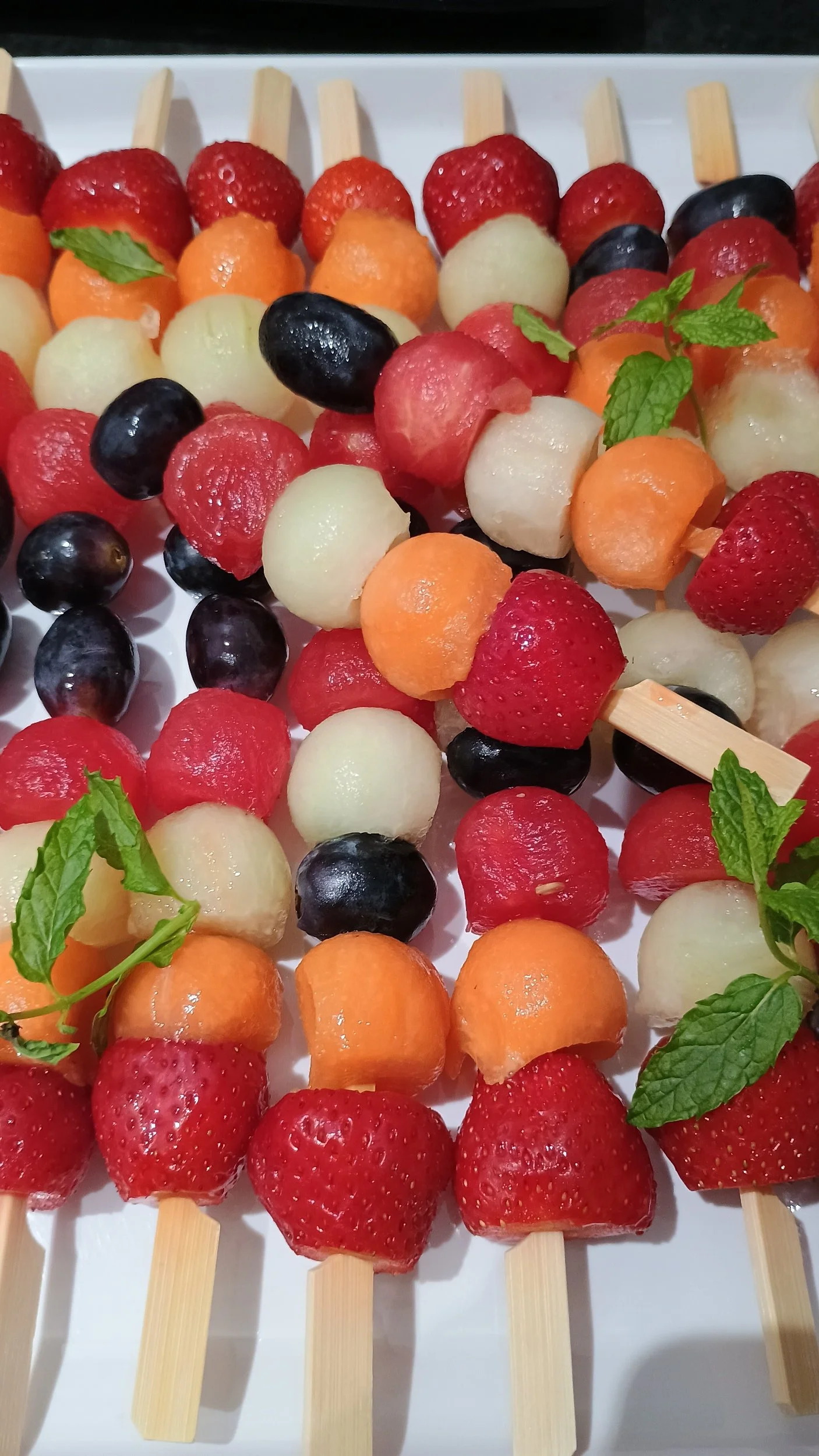 Assorted fruit skewers with strawberries, cantaloupe, honeydew, watermelon, grapes, and fresh mint leaves.