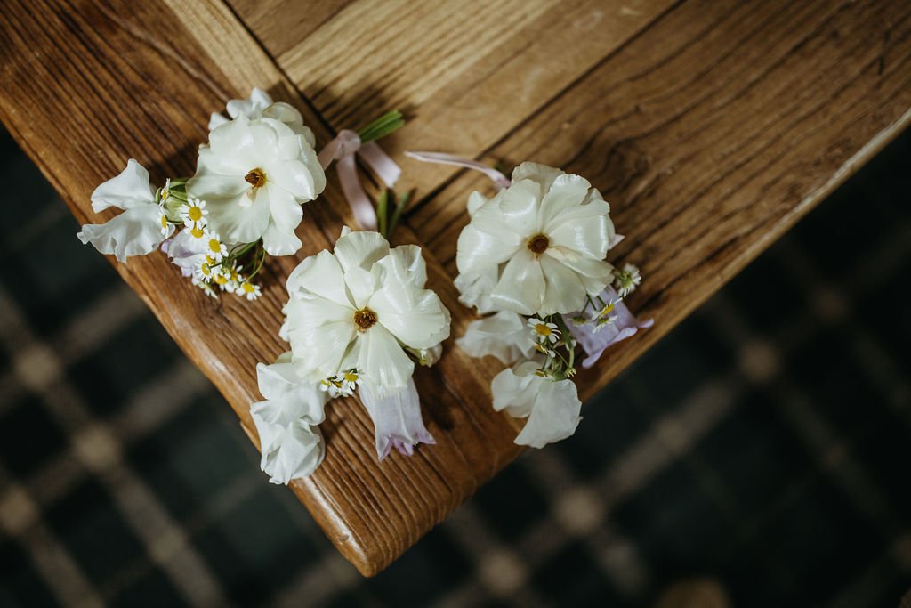 White and light purple flowers arranged on a wooden table edge.