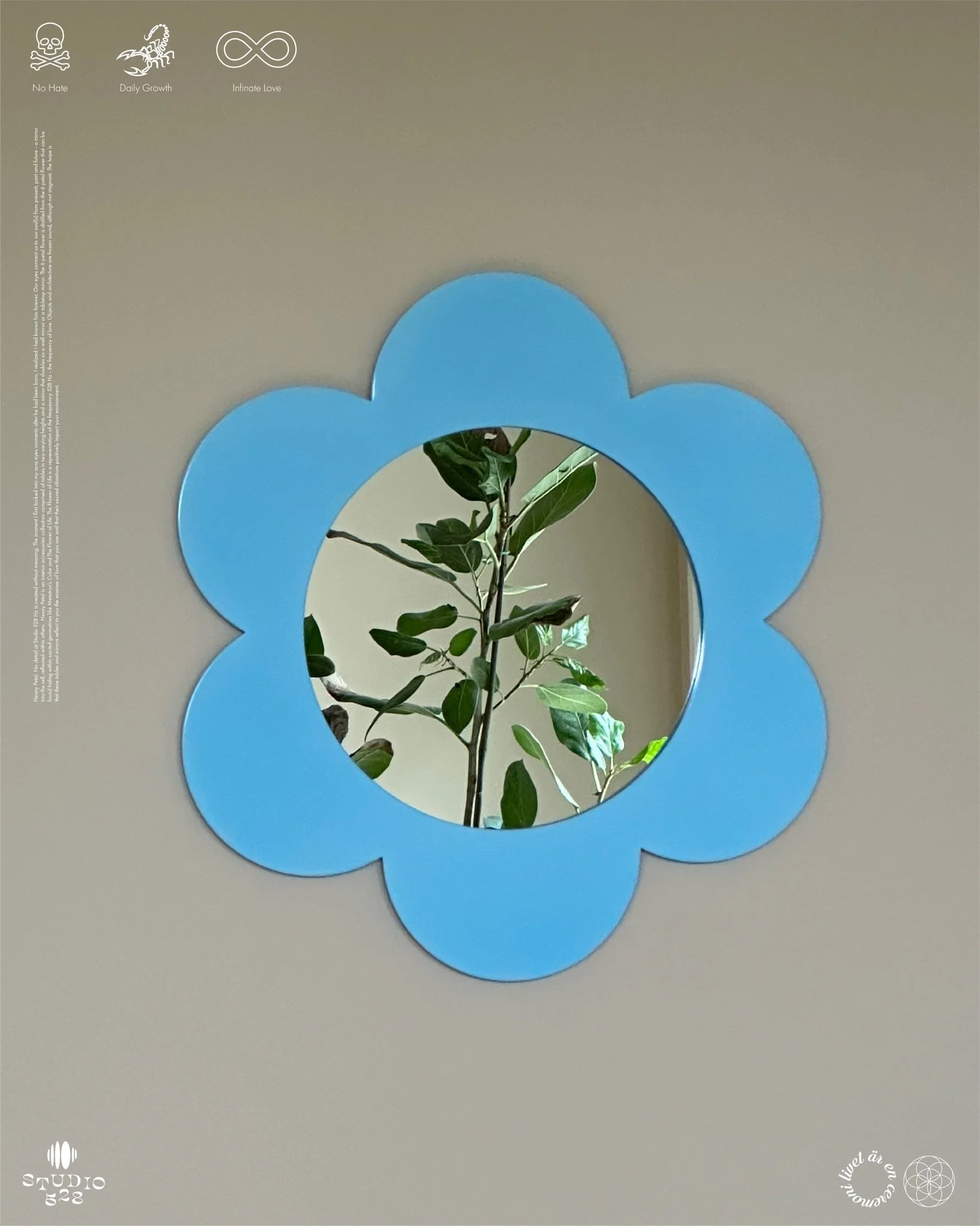 A mirror with a blue, flower-shaped frame reflects a branch with green leaves.