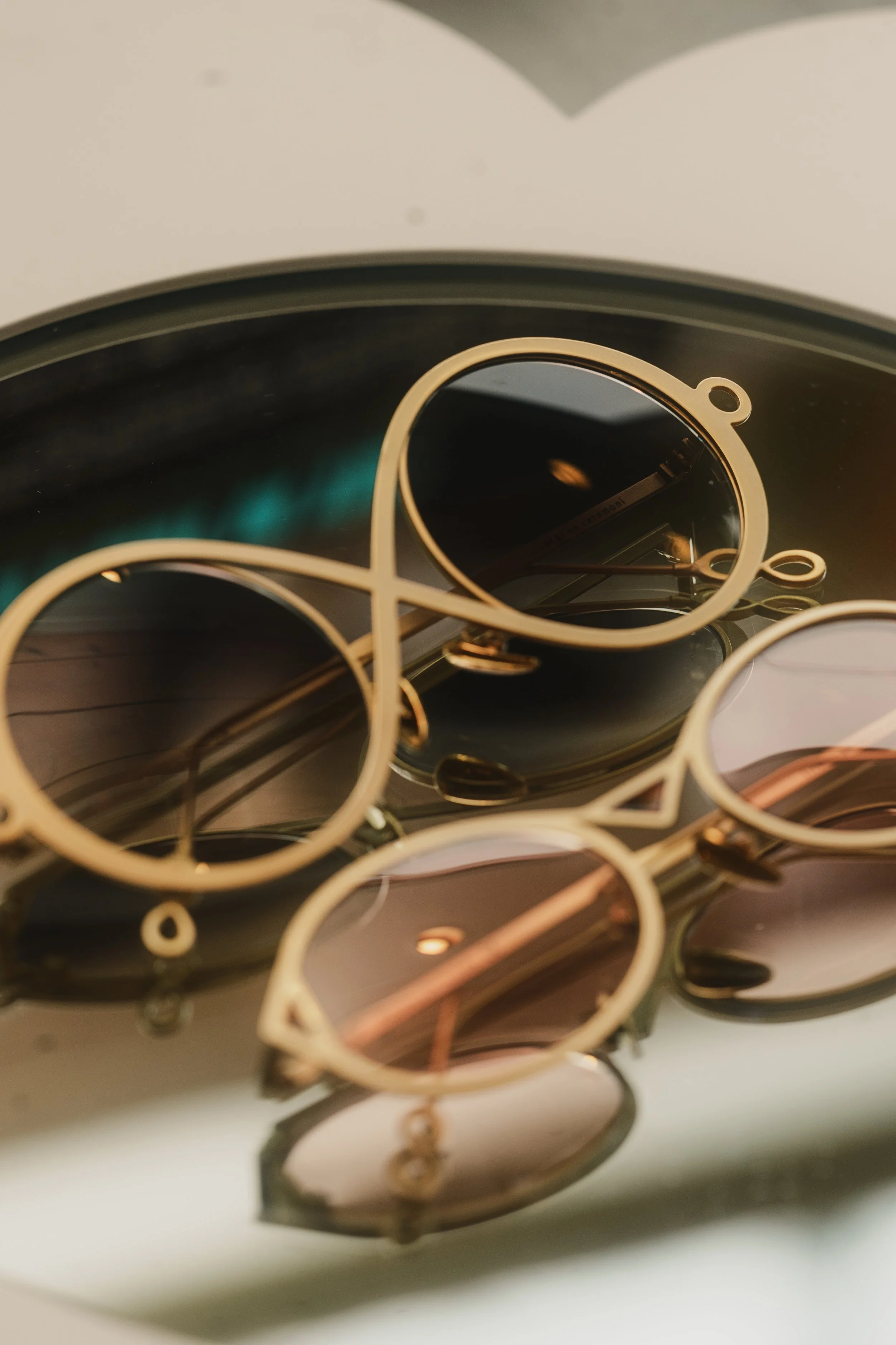 Close-up of multiple pairs of sunglasses with metallic frames and dark lenses, stacked together.