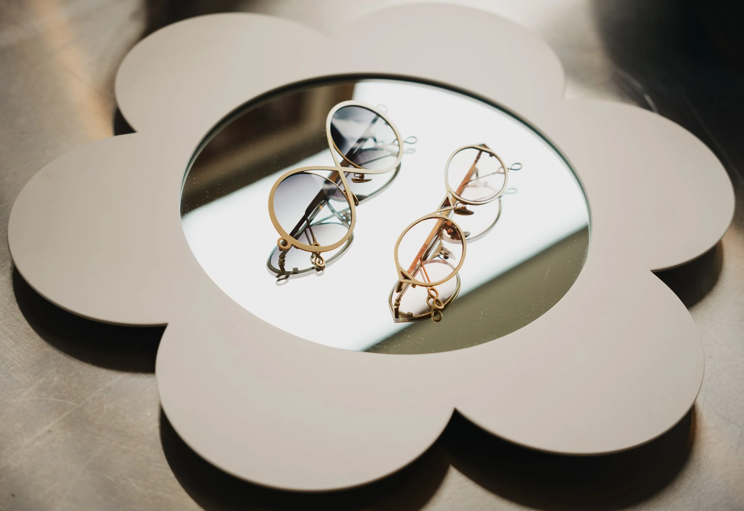 A decorative mirror with a floral shape holds three pairs of sunglasses on its reflective surface.