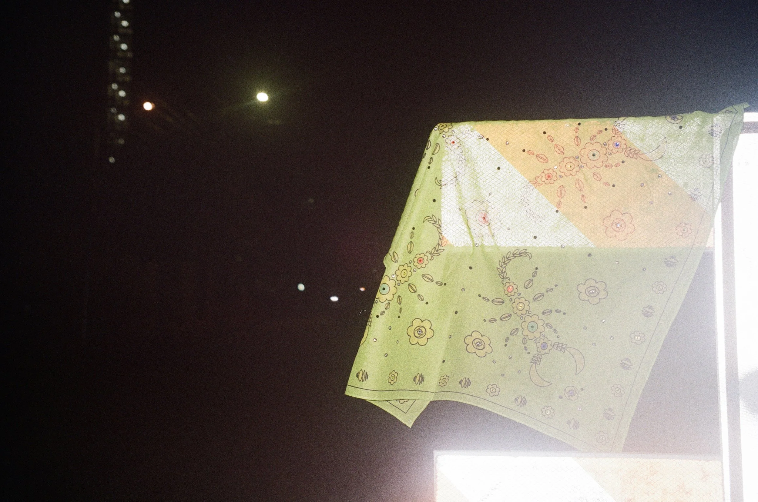 Colorful bandanas hanging in front of a dark night sky, with visible lights and the moon in the background.
