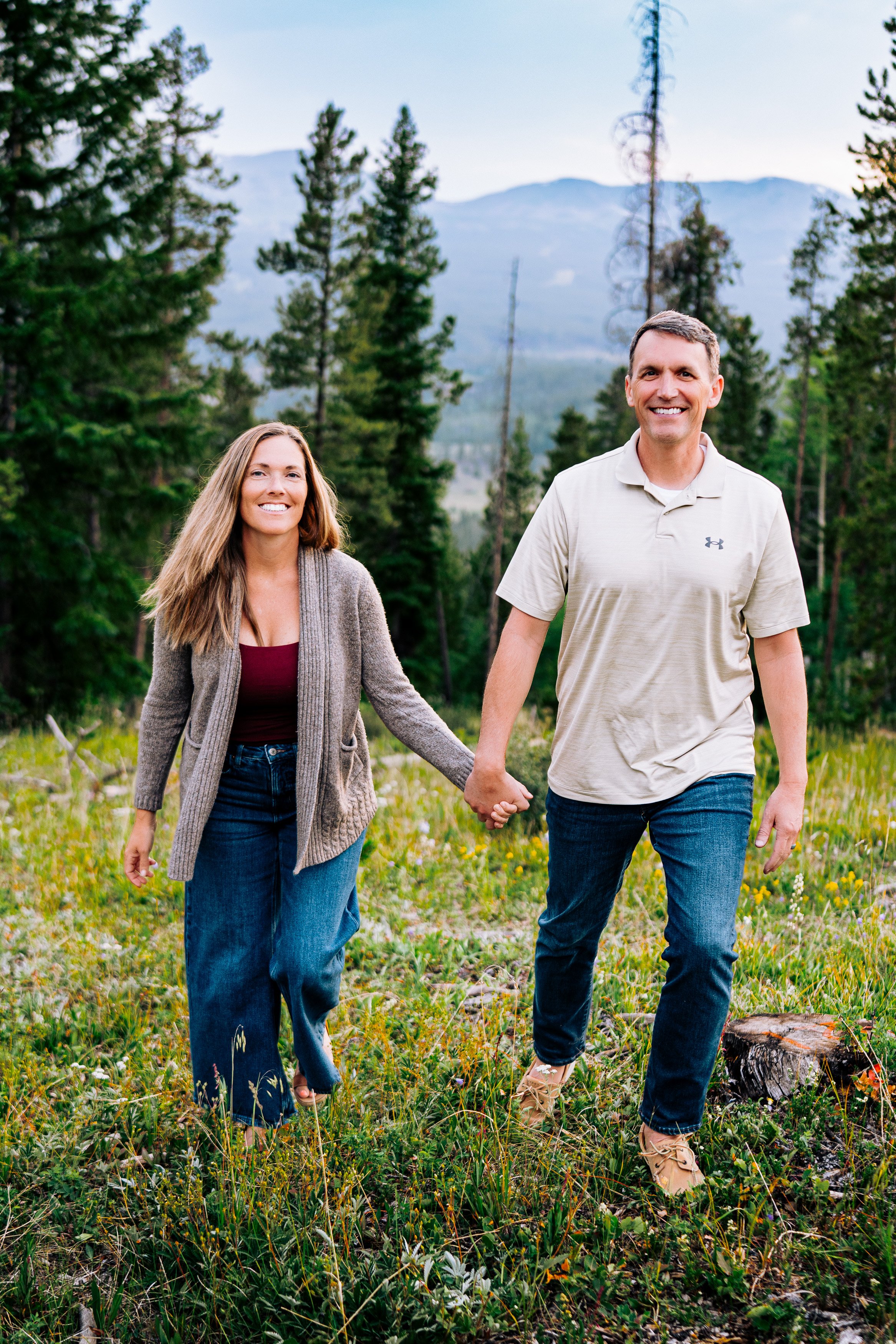 A breckenridge couple walking through a meadow of wildflowers with mountains.
