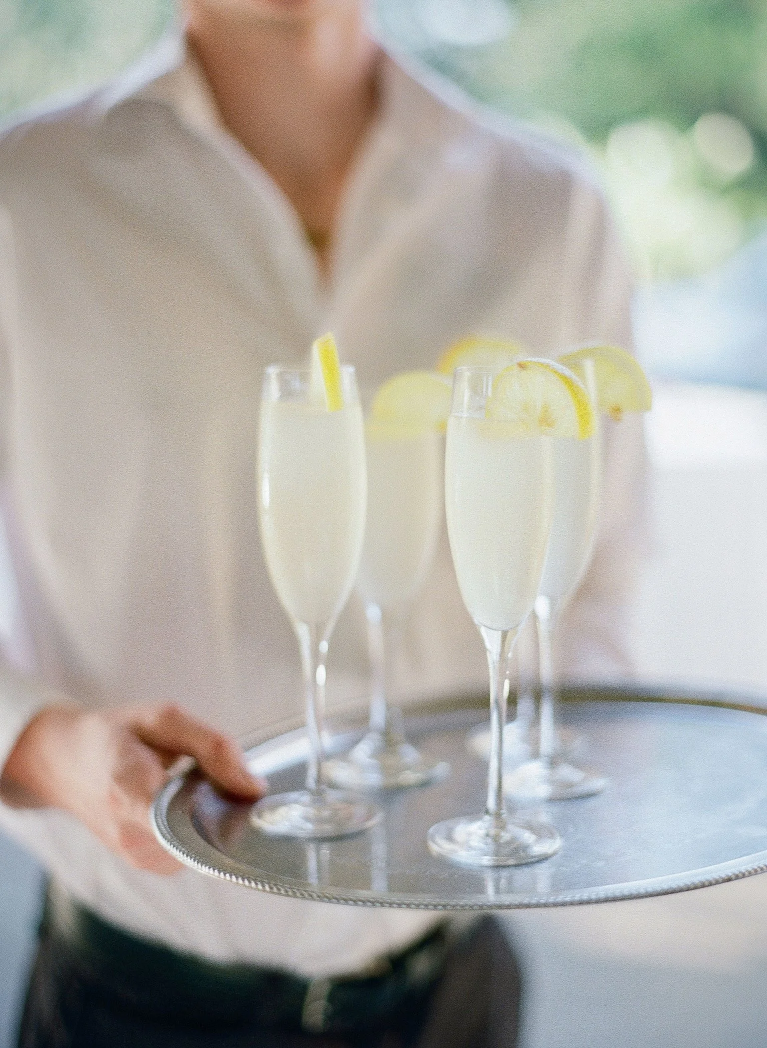 A server holding a tray with four glasses of lemonade garnished with lemon slices.