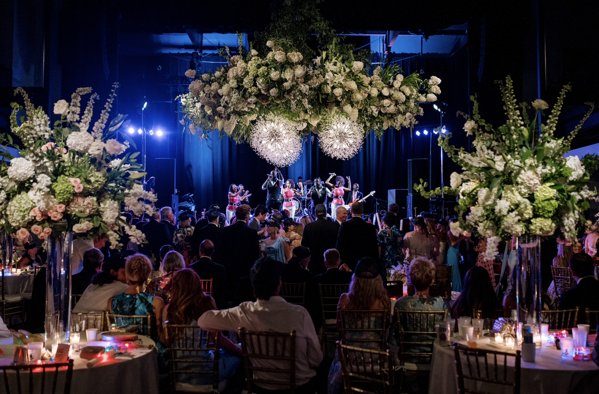 People attending a formal event with a live band and floral arrangements.
