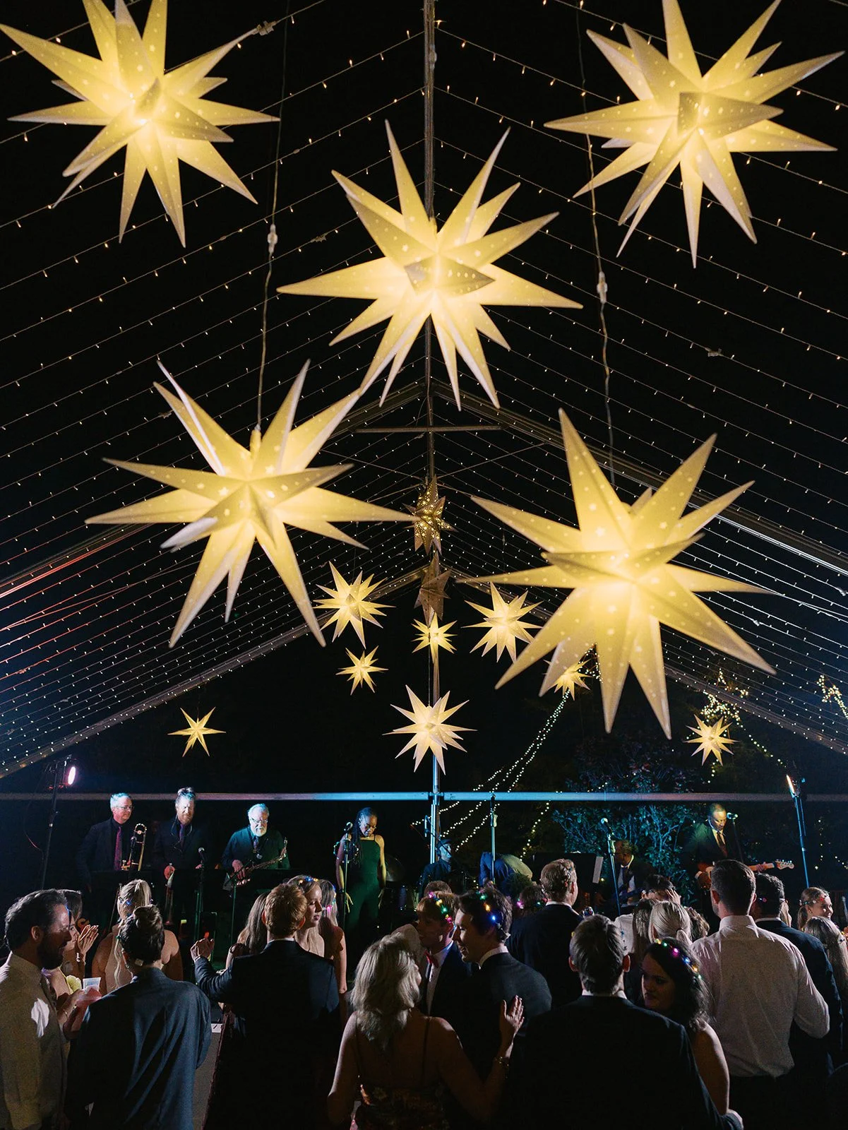 People dancing and socializing at an outdoor evening event decorated with large star-shaped lanterns and string lights.