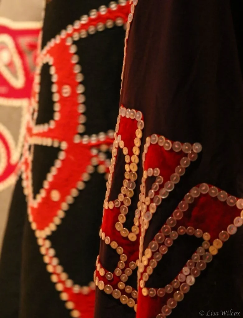Close-up of a decorated fabric with red, white, and black beads forming a pattern, possibly part of a jacket or costume.
