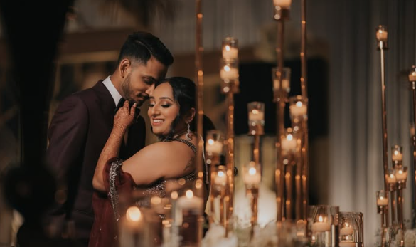 A couple smiling and embracing at a romantic event with candles and warm lighting.