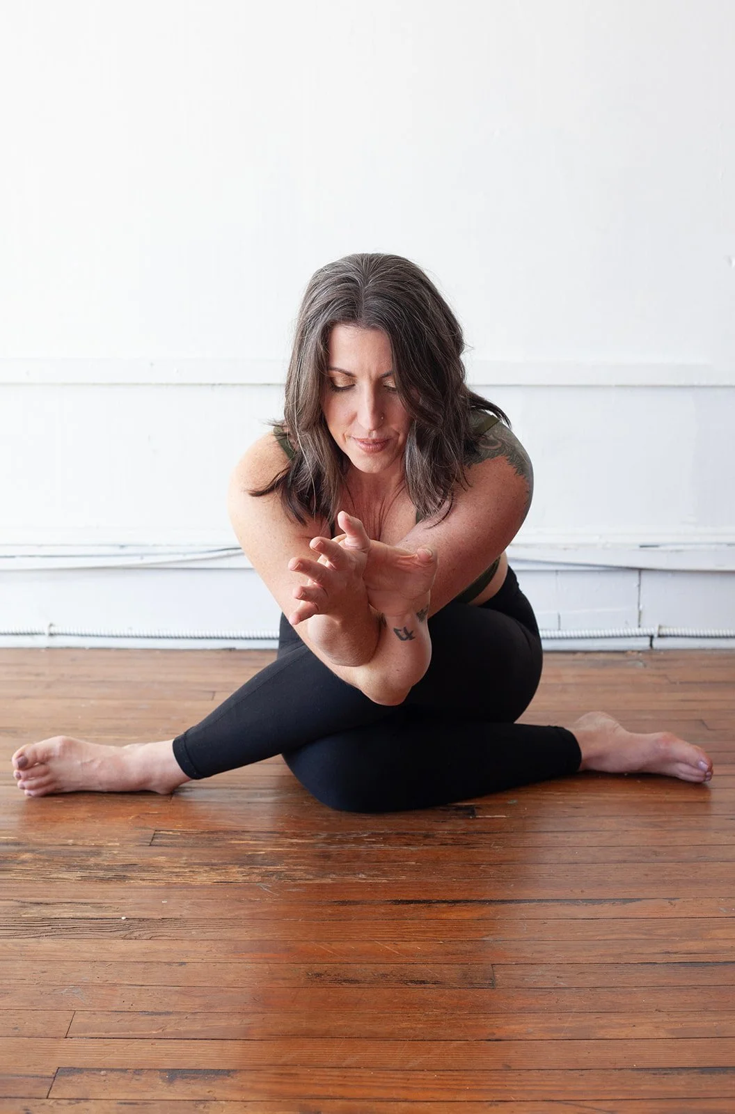 Woman practicing yoga indoors on wooden floor, sitting in a seated twist pose, with her eyes closed and focused.