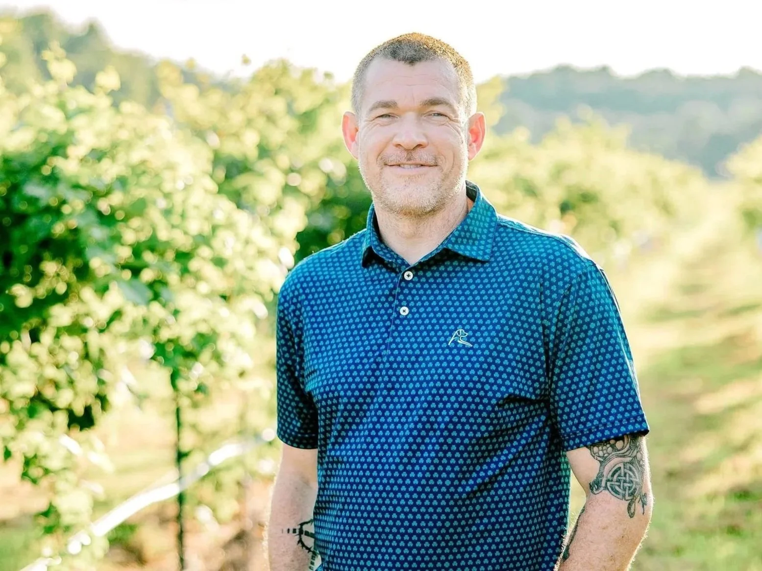 A man with short dark hair and a blue polo shirt standing in a vineyard