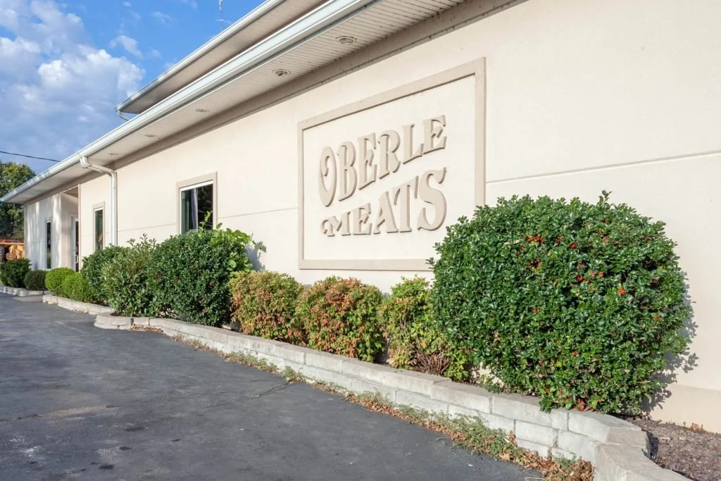 cream colored building with green bushes lining it. Sign on wall says Oberle Meats