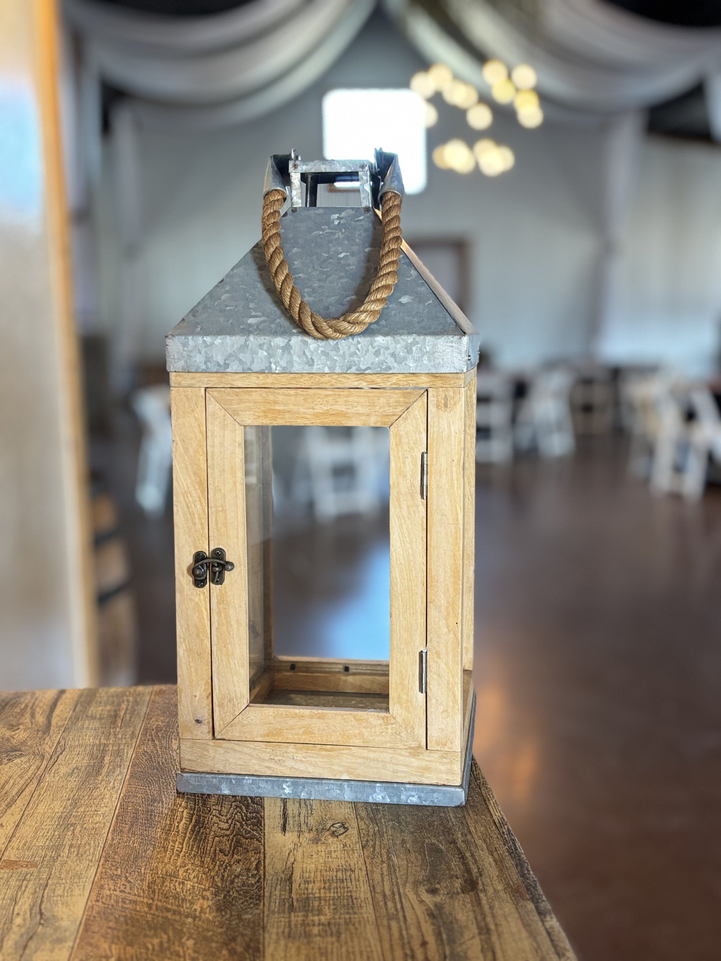 Wood and metal lantern with glass panels and a small door, placed on a wooden table in a decorated indoor space.