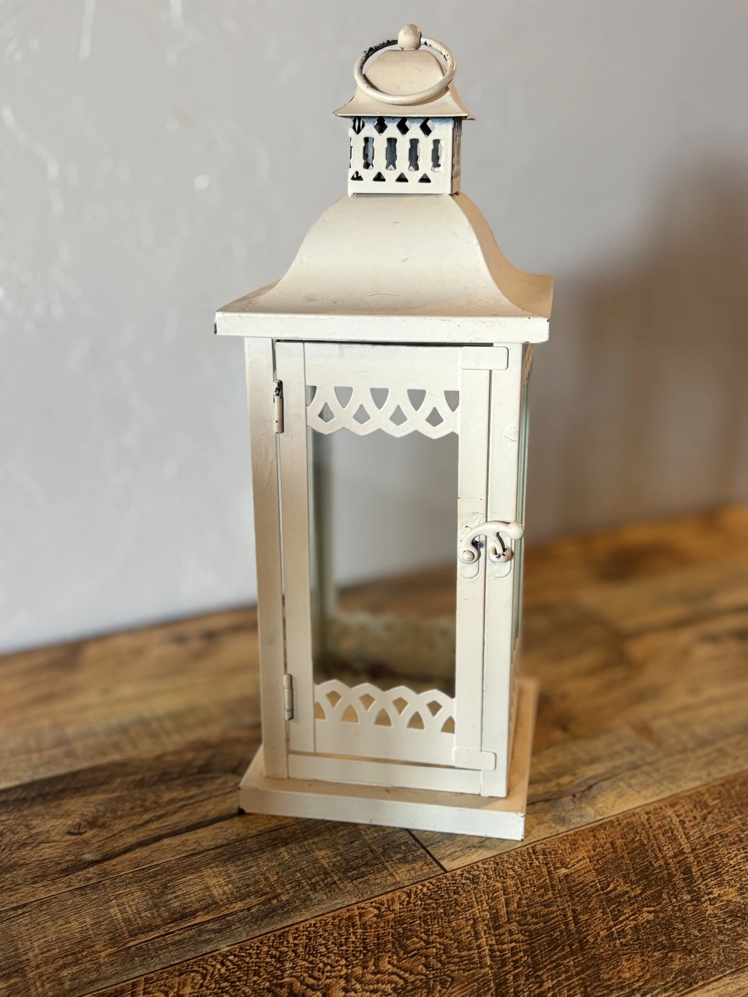 White decorative lantern with a small door and reflective glass panel on a wooden surface.
