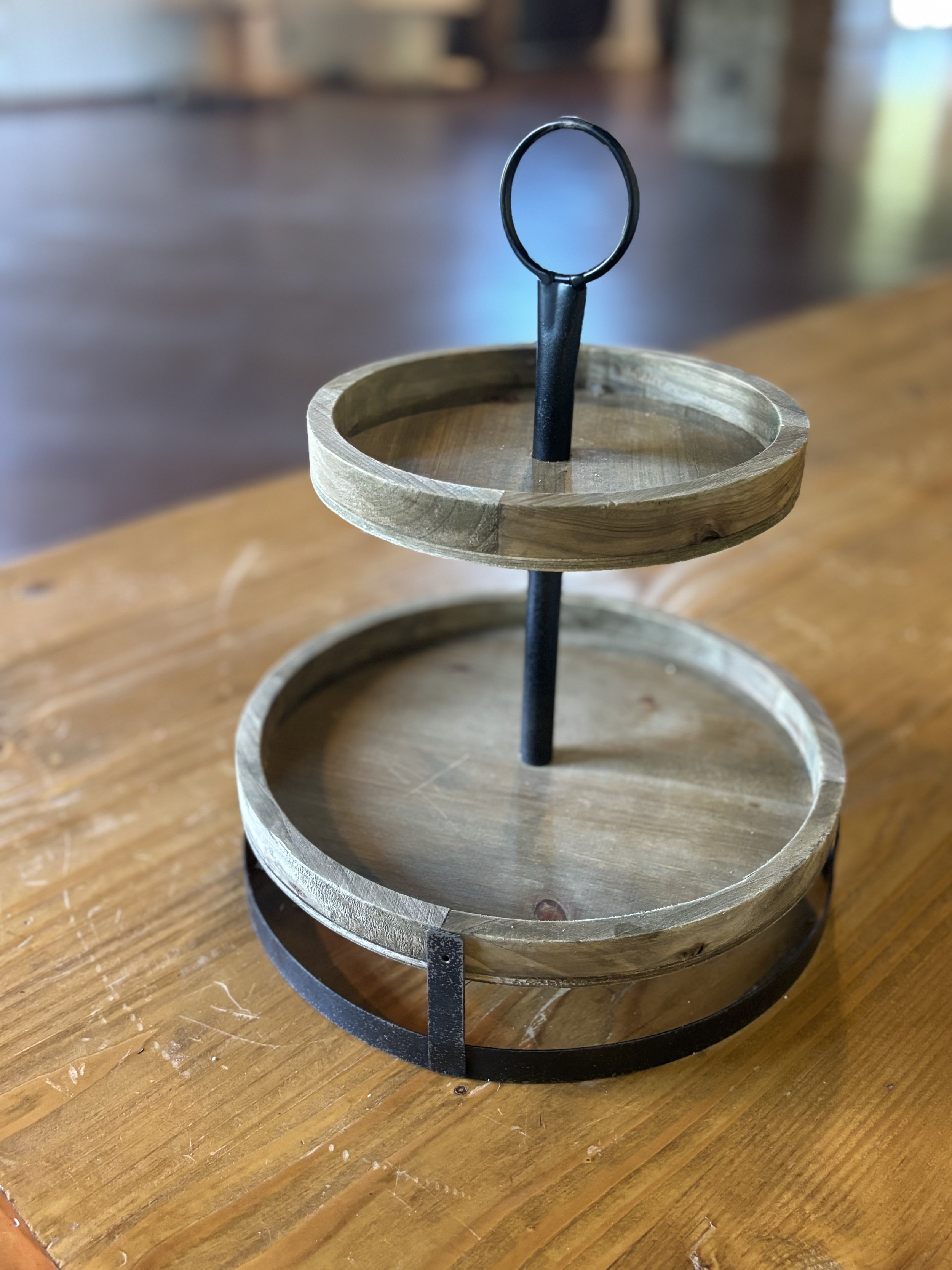 A two-tier wooden tray with a metal handle in the center, placed on a wooden table.