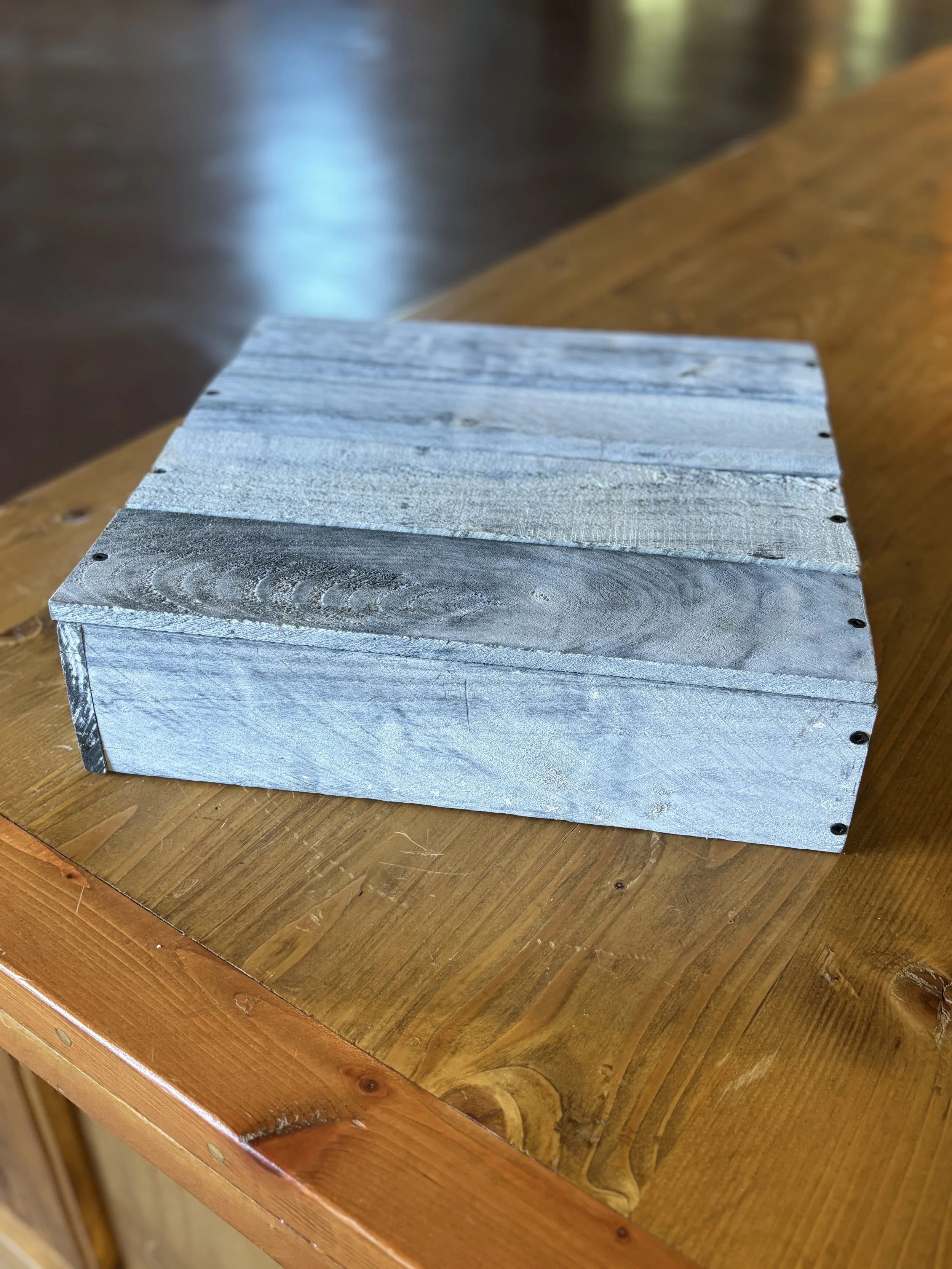 A rectangular wooden box painted in shades of blue and gray, placed on a wooden table.