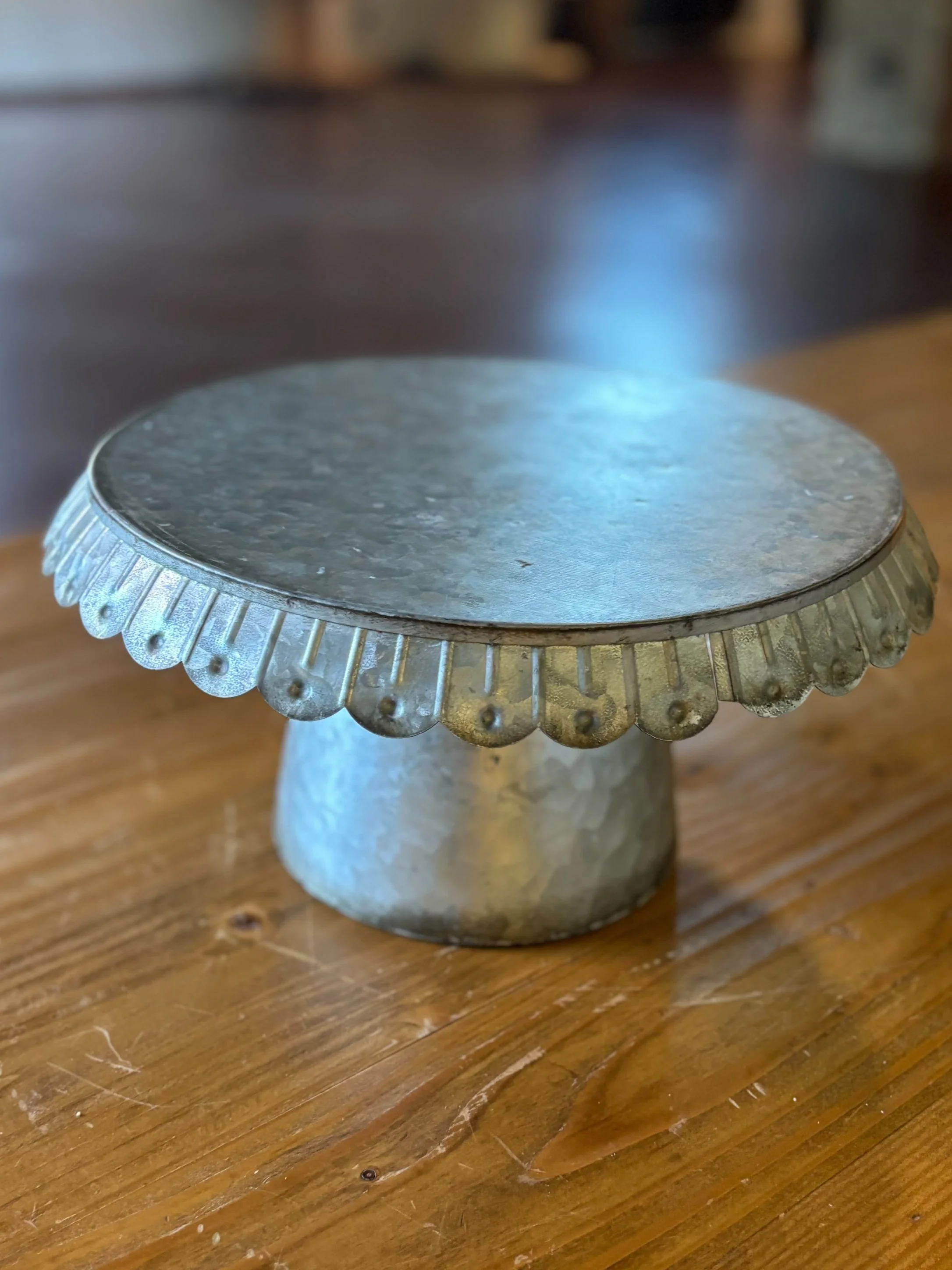 A small, metallic, decorative cake stand with a scalloped edge, placed on a wooden surface.
