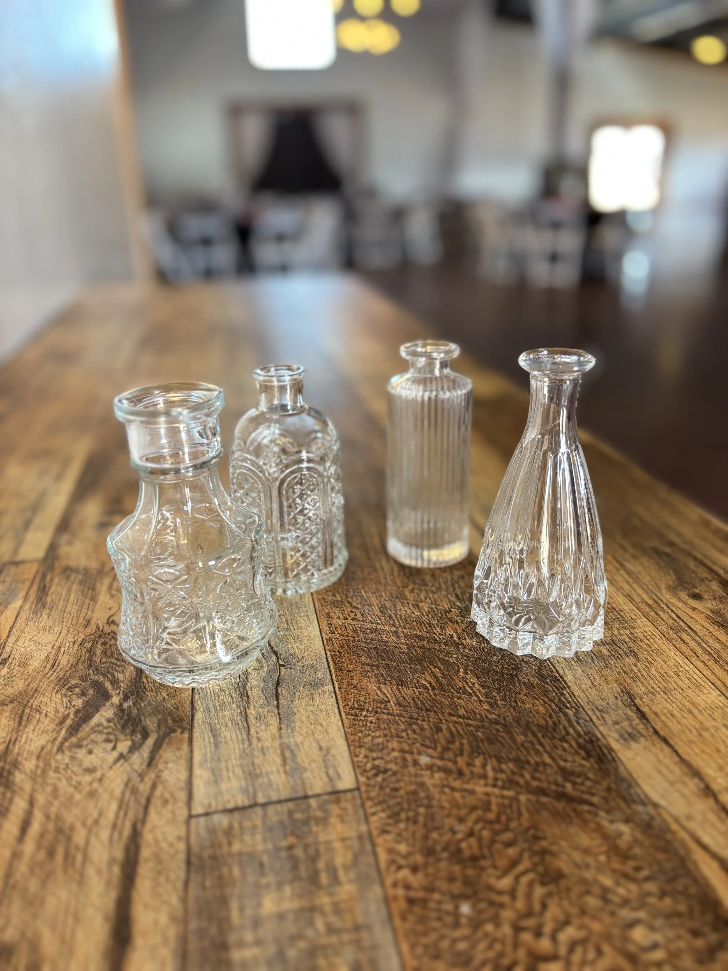 Four small glass vases with intricate designs on a wooden table in a blurred background of a cozy room.