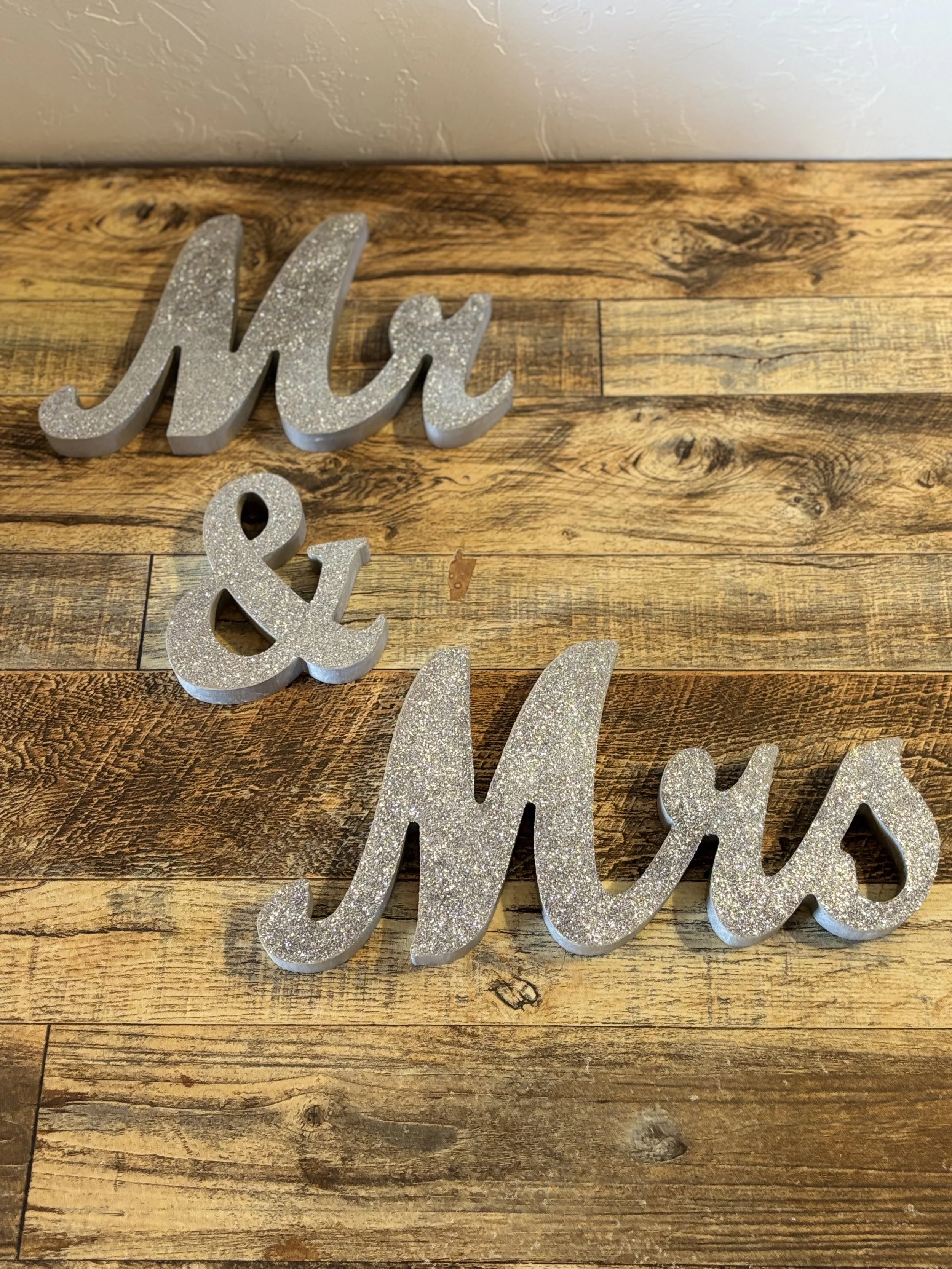 Decorative silver glittered sign spelling 'Mr & Mrs' on a wooden surface.