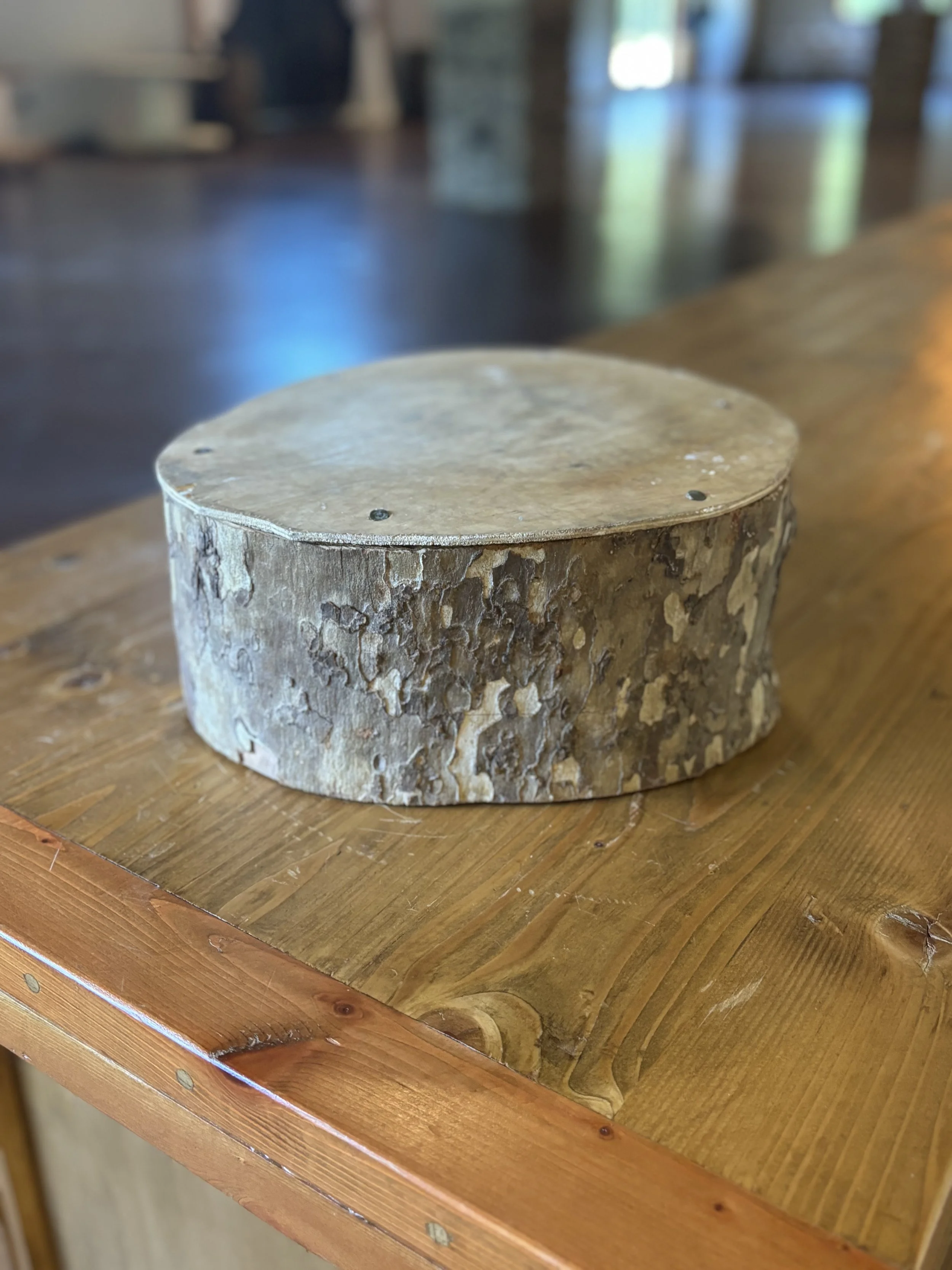 A round wooden percussion instrument, possibly a log drum, placed on a wooden table indoors.