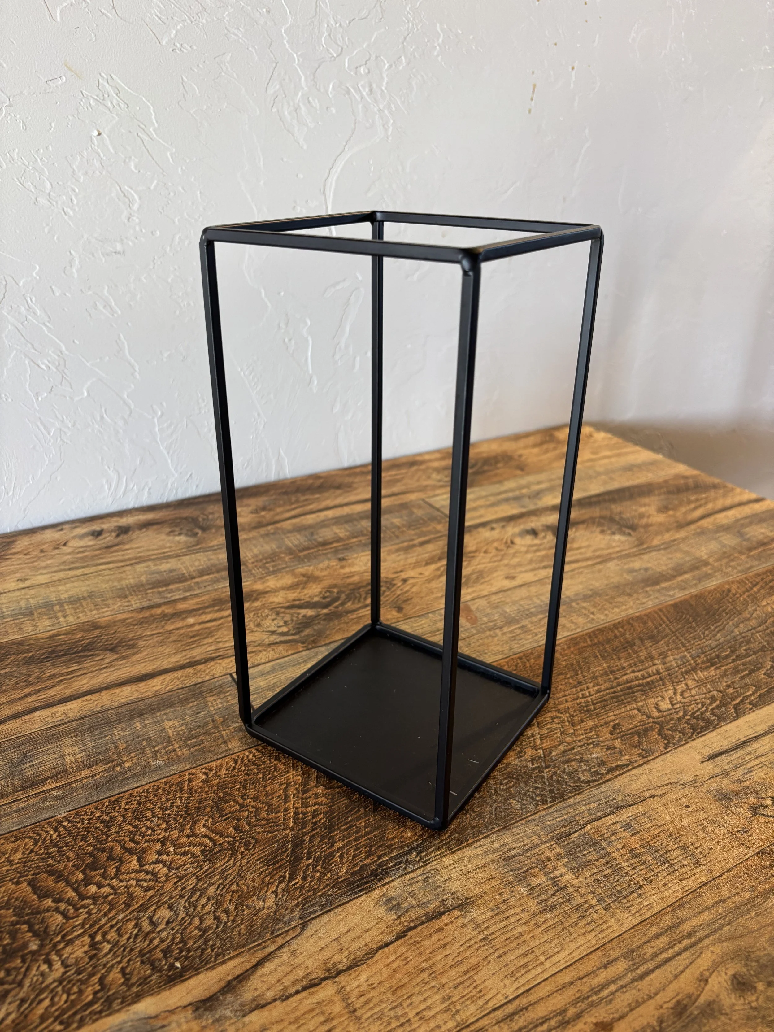 Black metal rectangular frame with open sides and a flat base, placed on a wooden surface.
