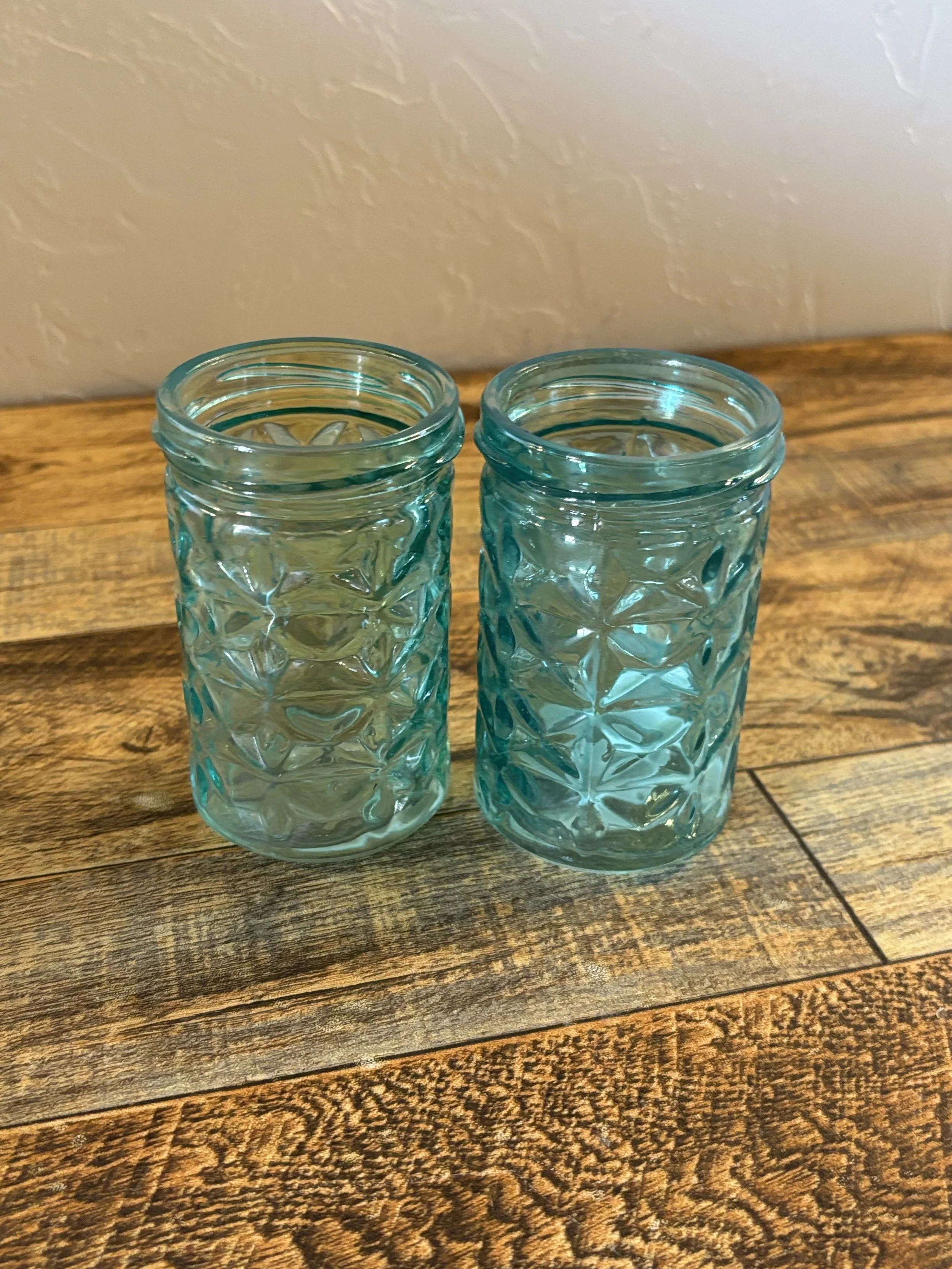 Two textured glass jars on a wooden surface against a plain wall.