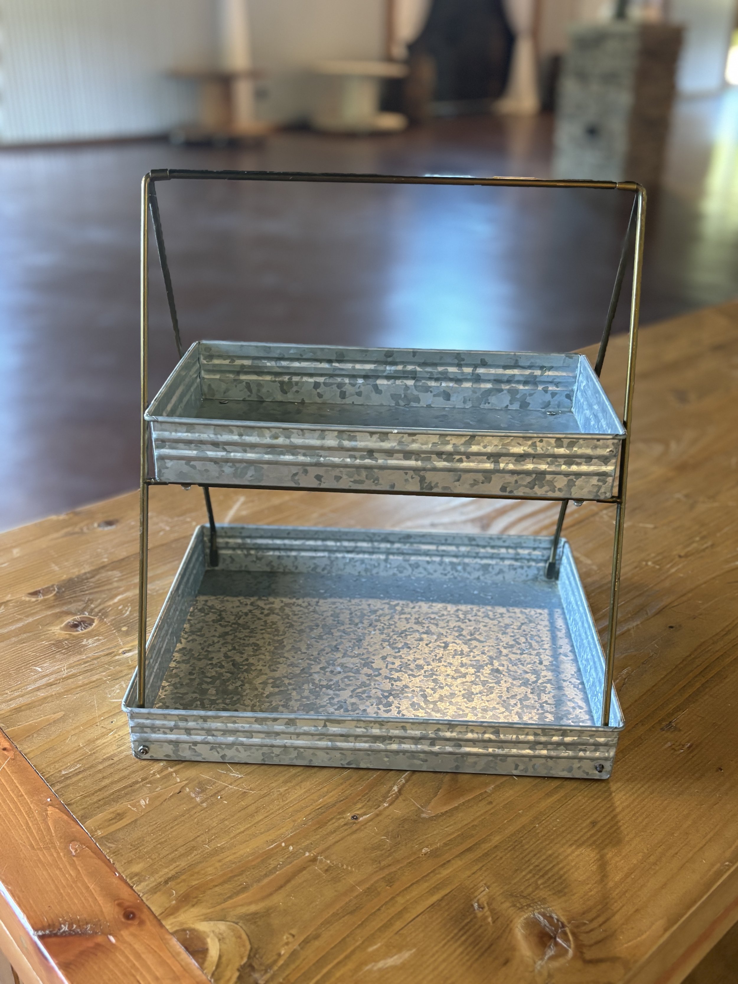 A 2-tier galvanized metal plant stand with a wooden surface.